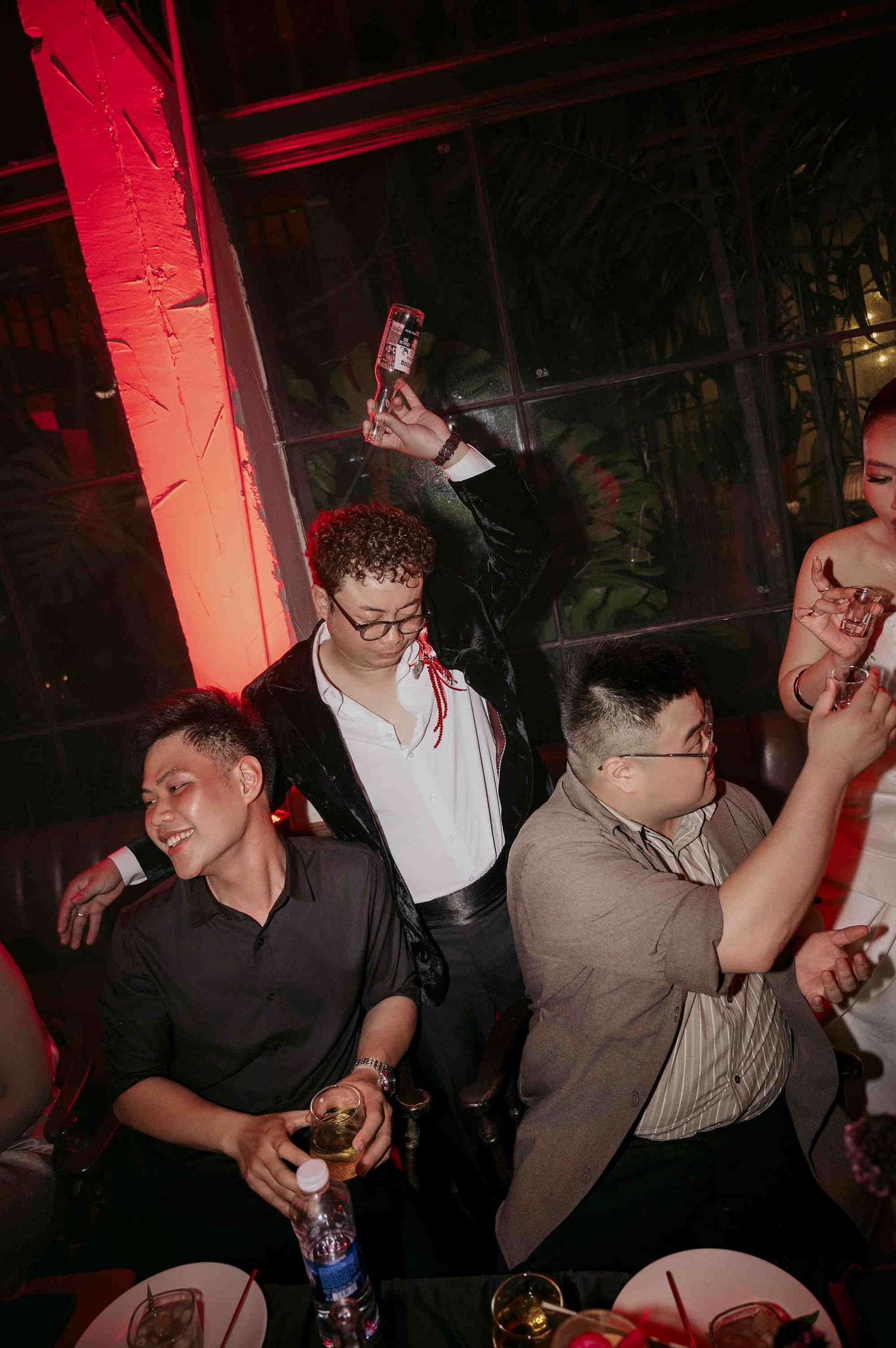 Group of friends celebrating at a nightclub party, with one person holding up a phone camera under red ambient lighting.
