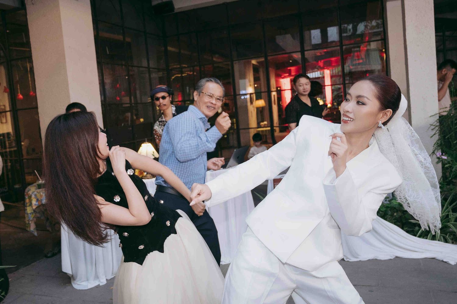 Elegant wedding scene with bride in white suit and veil dancing with guests outdoors at a venue.