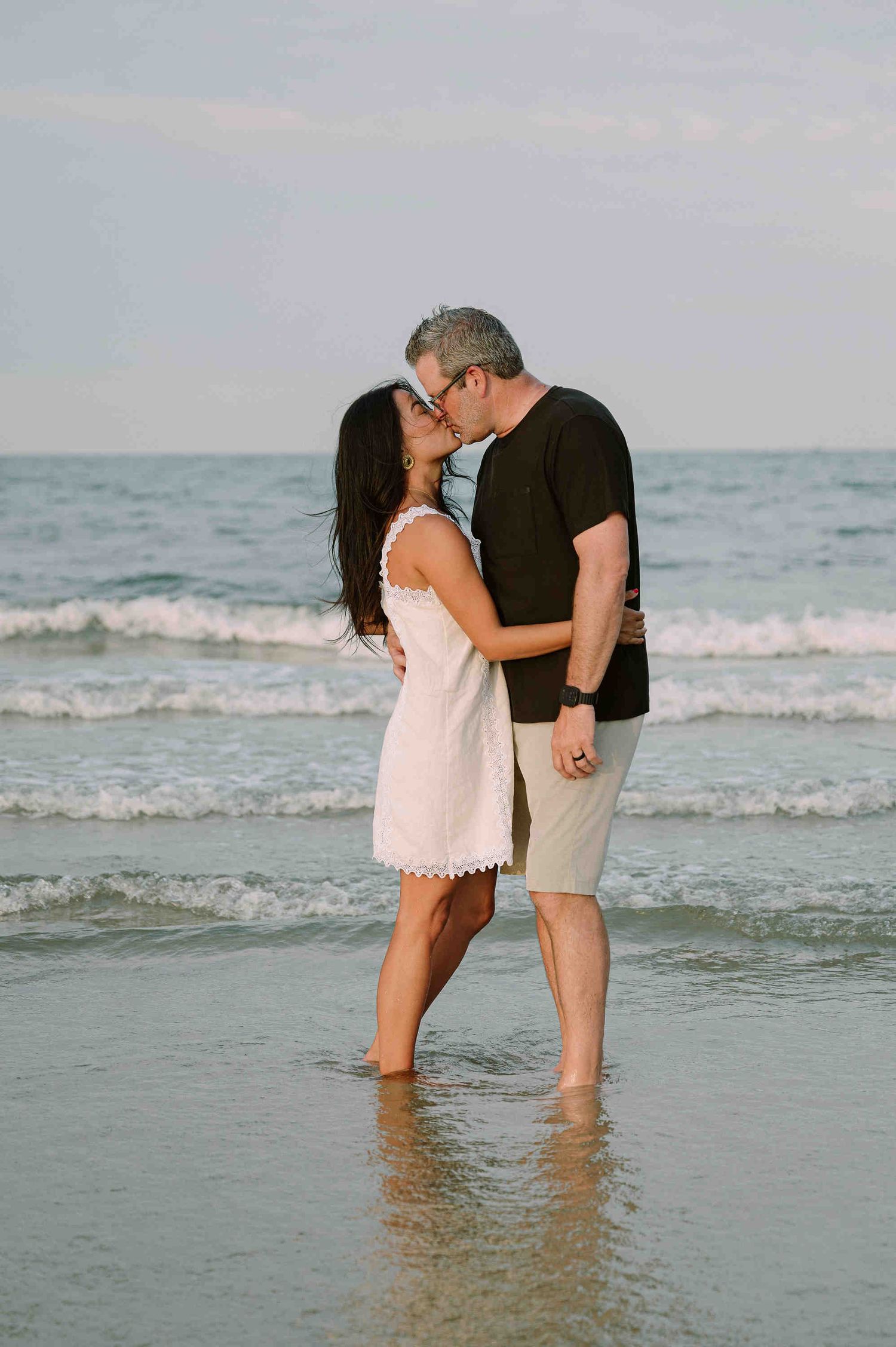 Da Nang family: couple shares a romantic moment while standing in the shallow ocean waves at the beach, by AnhVuWedding.