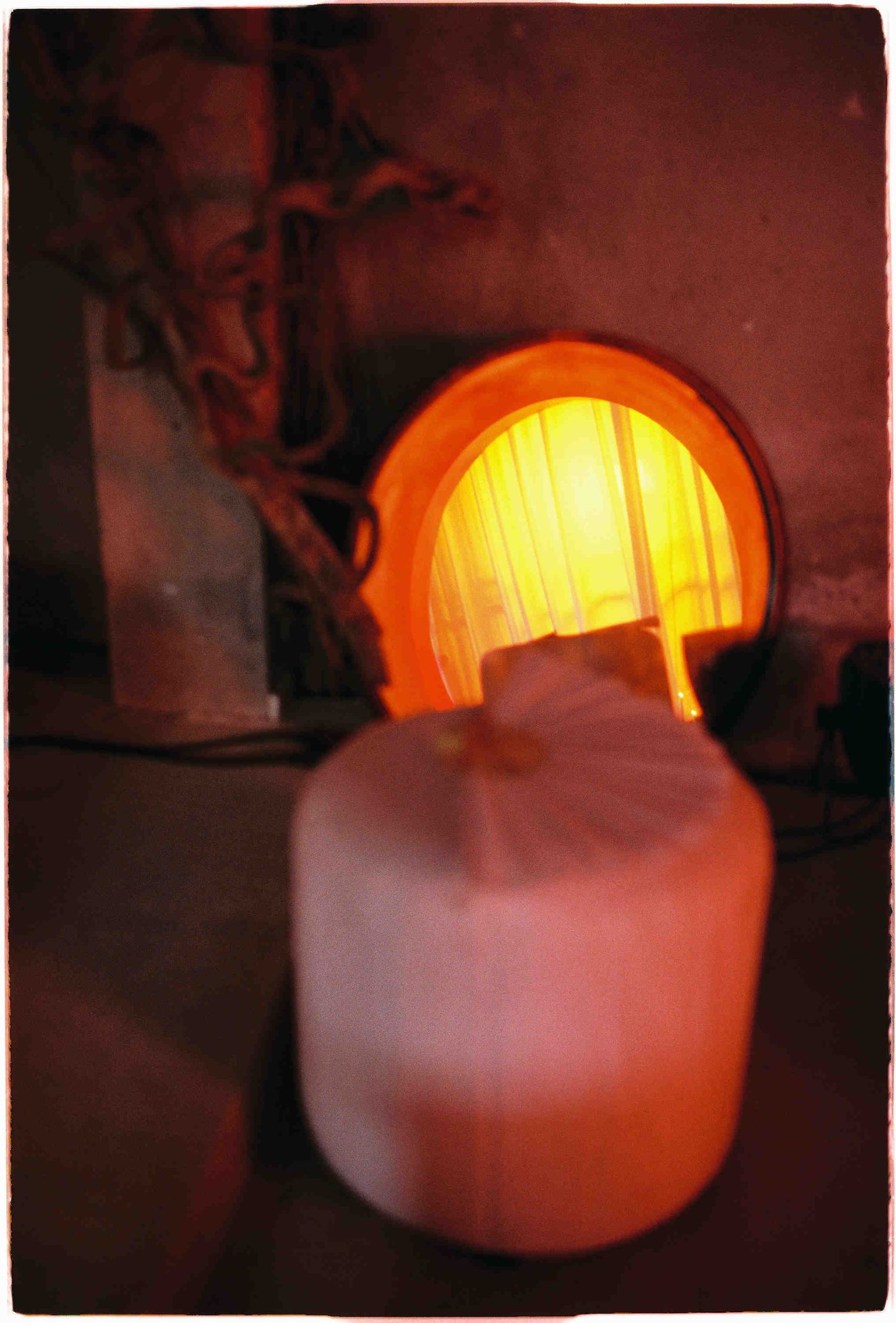A glowing kiln furnace with intense orange light illuminating a white ceramic vessel being fired in a pottery studio.