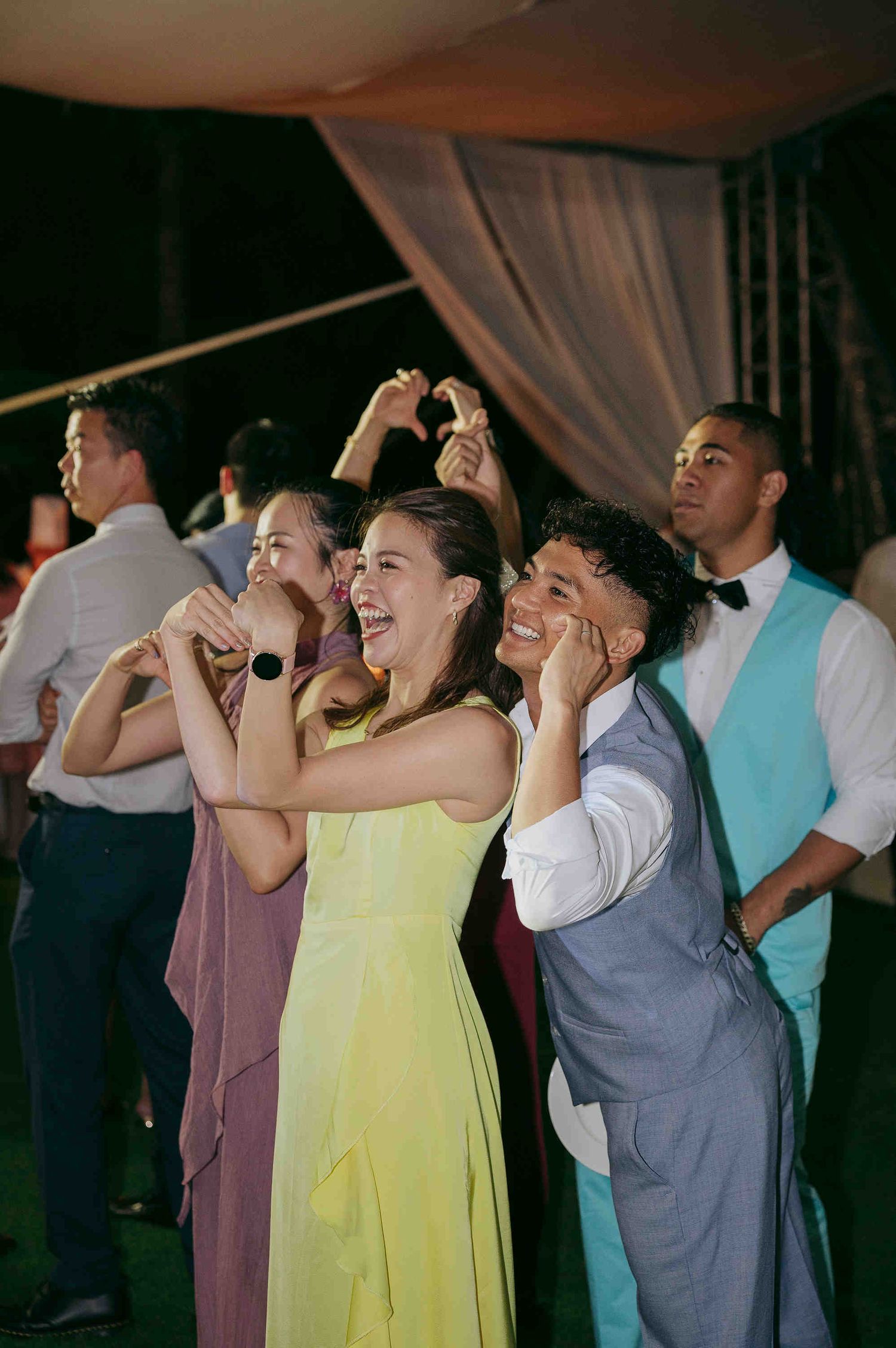 Guests in formal attire laughing and dancing joyfully at an outdoor wedding reception celebration.