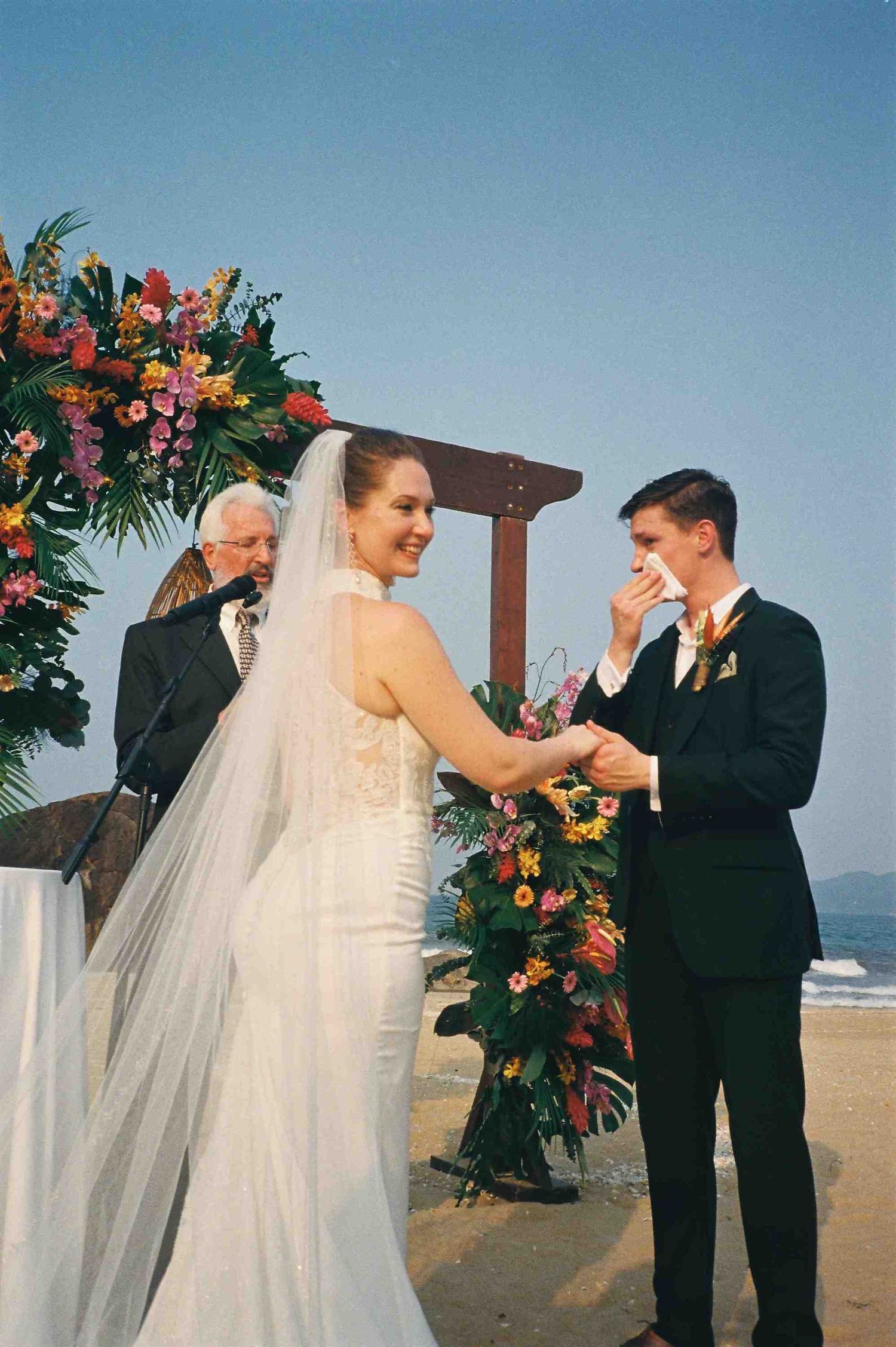 Lang Co wedding ceremony: wedding couple exchanges rings during beach ceremony under floral-adorned wooden arch, by AnhVuWedding.