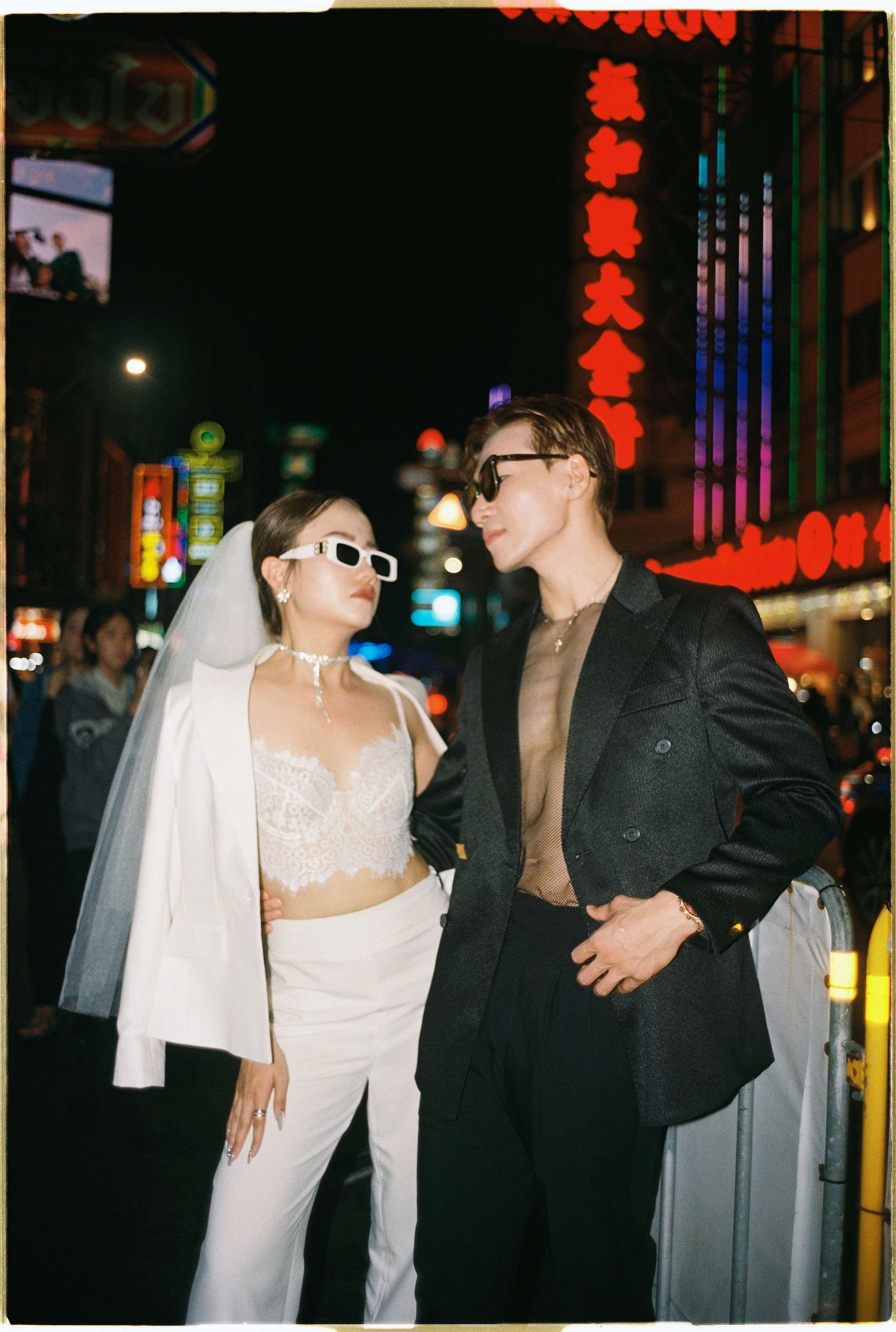 Saigon pre-wedding: two people in contrasting black and white outfits pose on a city street at night with red lanterns, by AnhVuWedding.