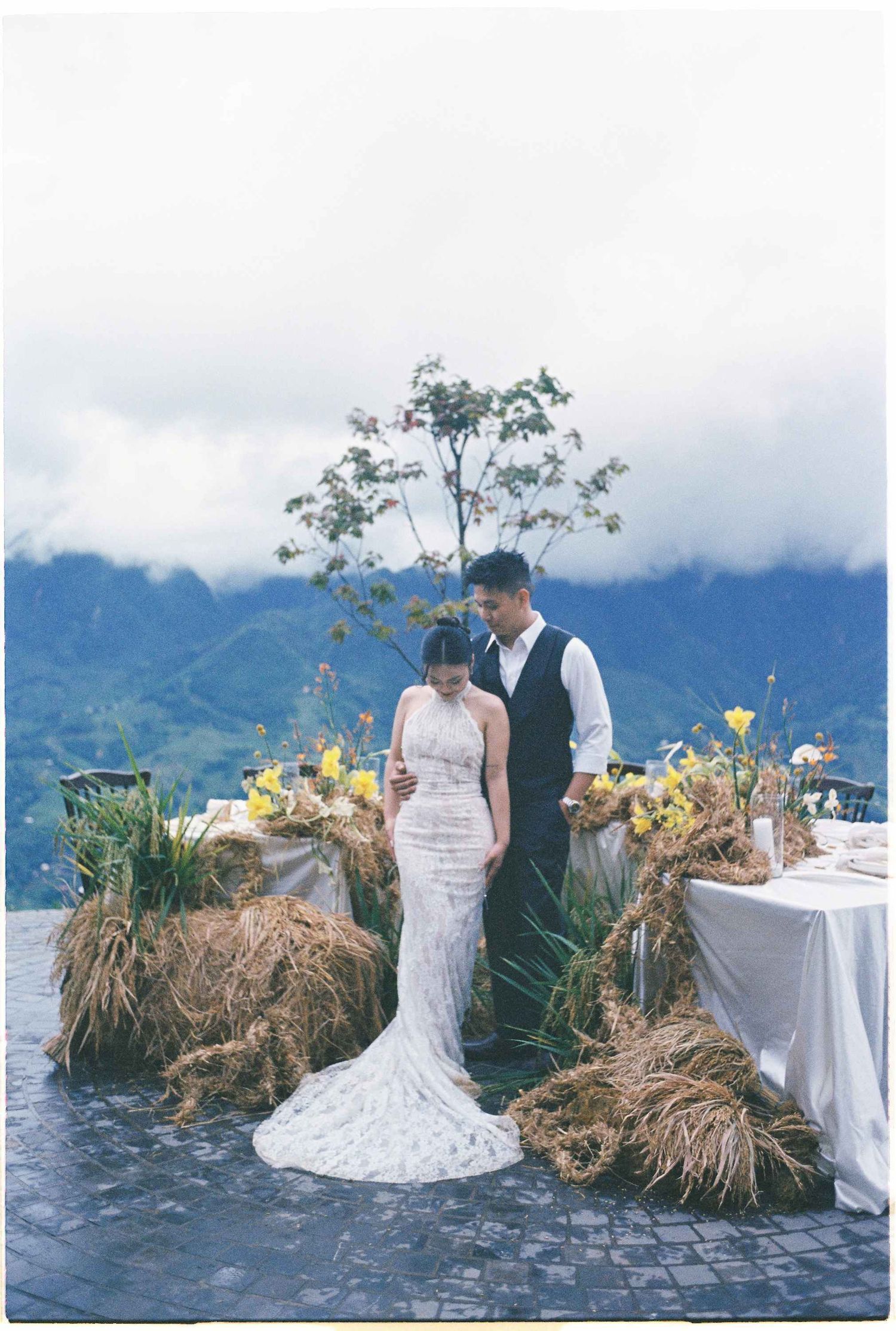 wedding: wedding couple poses near decorated tables on stone patio with mountain backdrop, by AnhVuWedding.