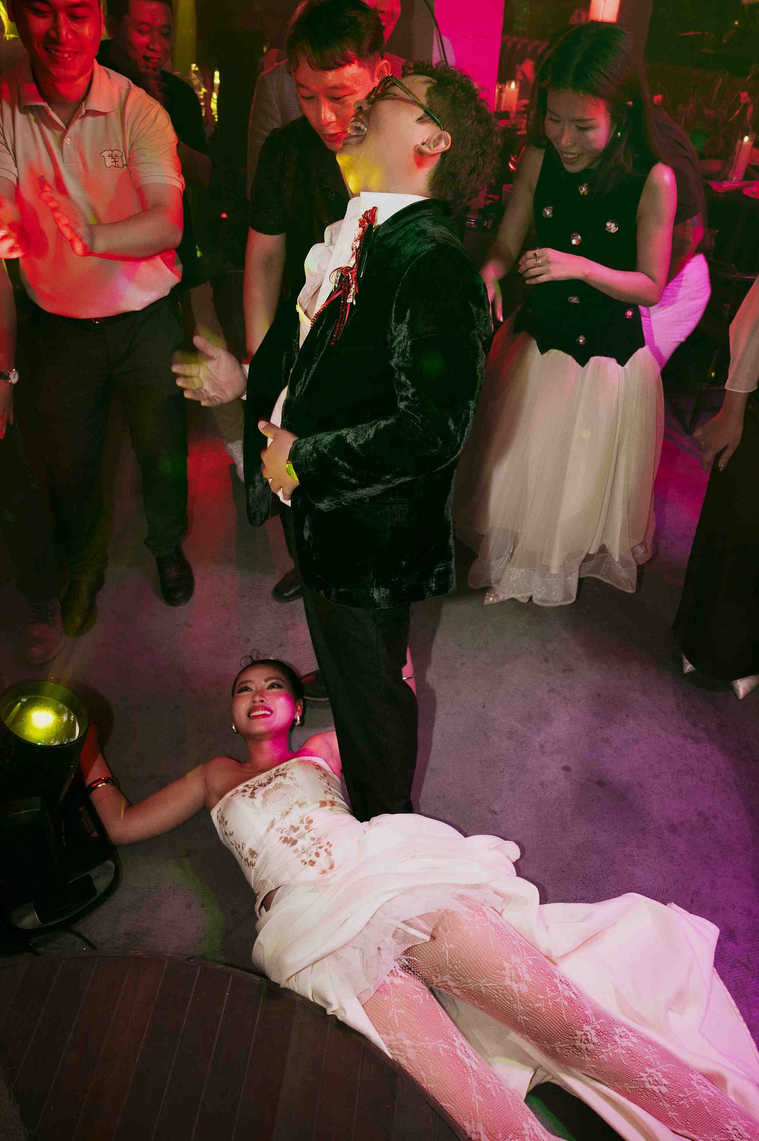 People dancing at a party, with a woman in a white dress on the floor and a man in a velvet suit leaning back.