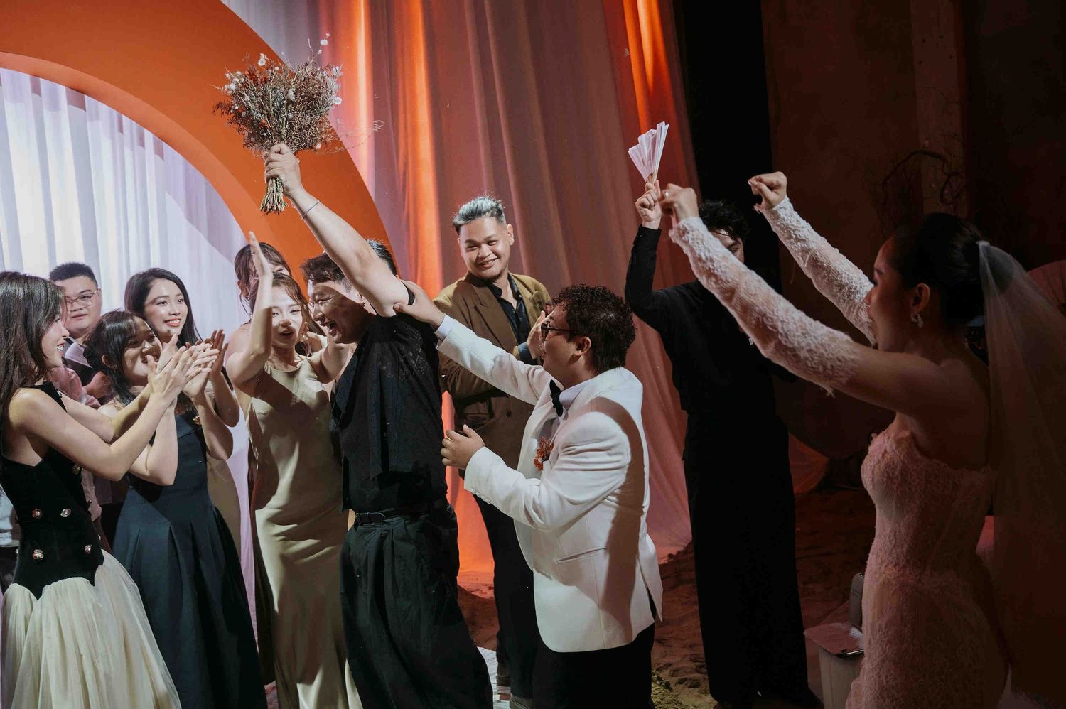 Wedding guests celebrate as bride tosses bouquet at elegant indoor reception ceremony.