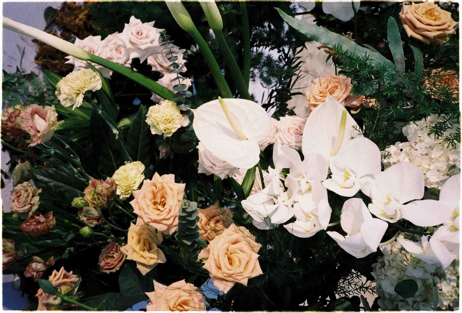 Elegant floral arrangement featuring white calla lilies, peach roses, and lush greenery for weddings or events.