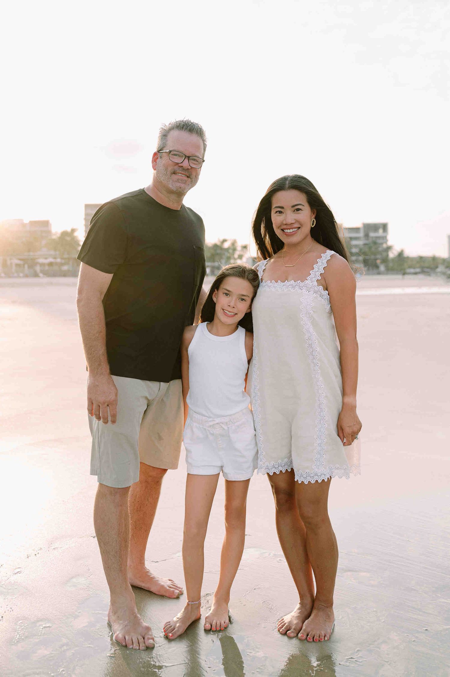 Da Nang family: family of three stands barefoot on a beach at sunset, by AnhVuWedding.