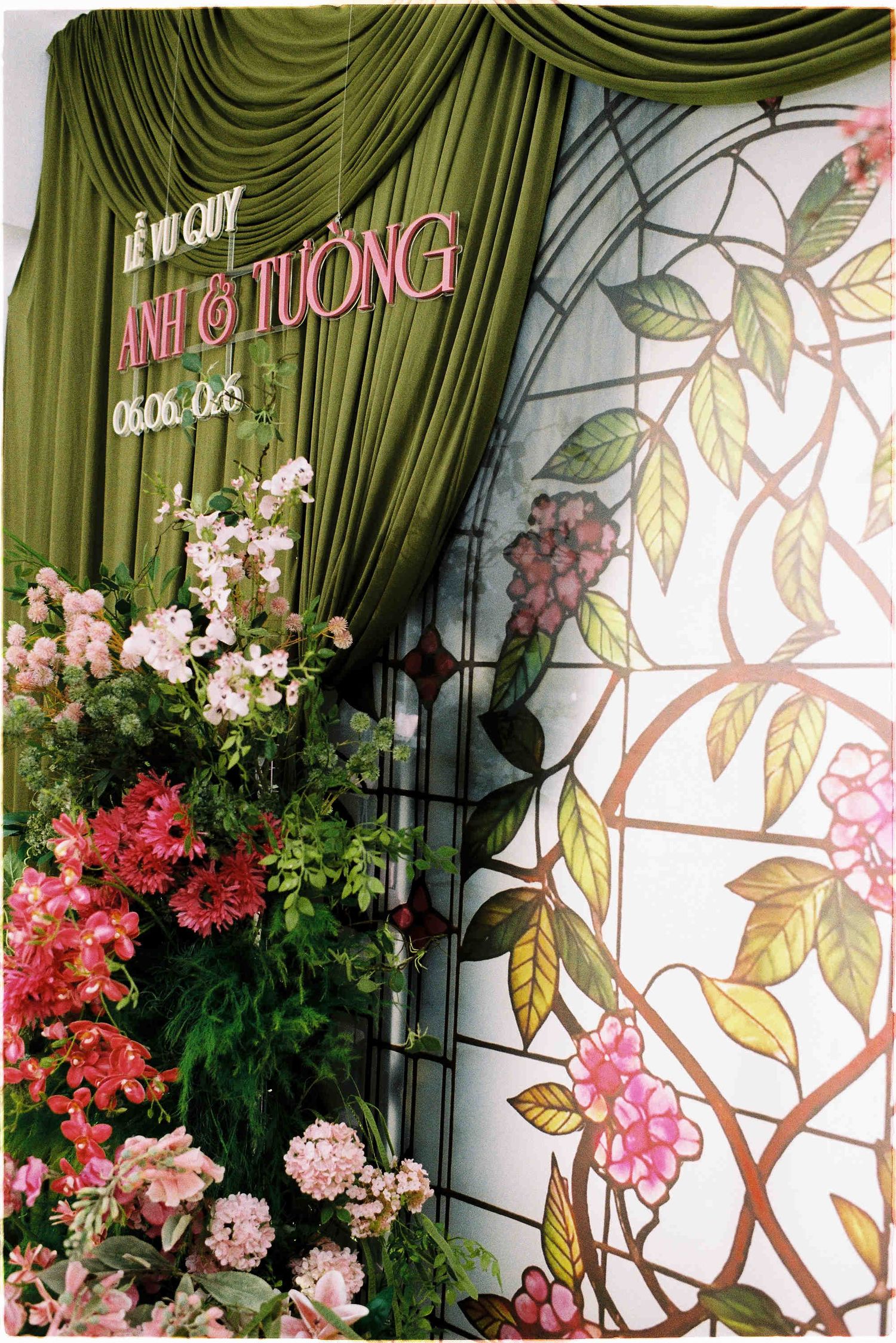 Vietnamese wedding backdrop with green drapes, pink flowers, and stained glass floral panel for Anh and Tuong.