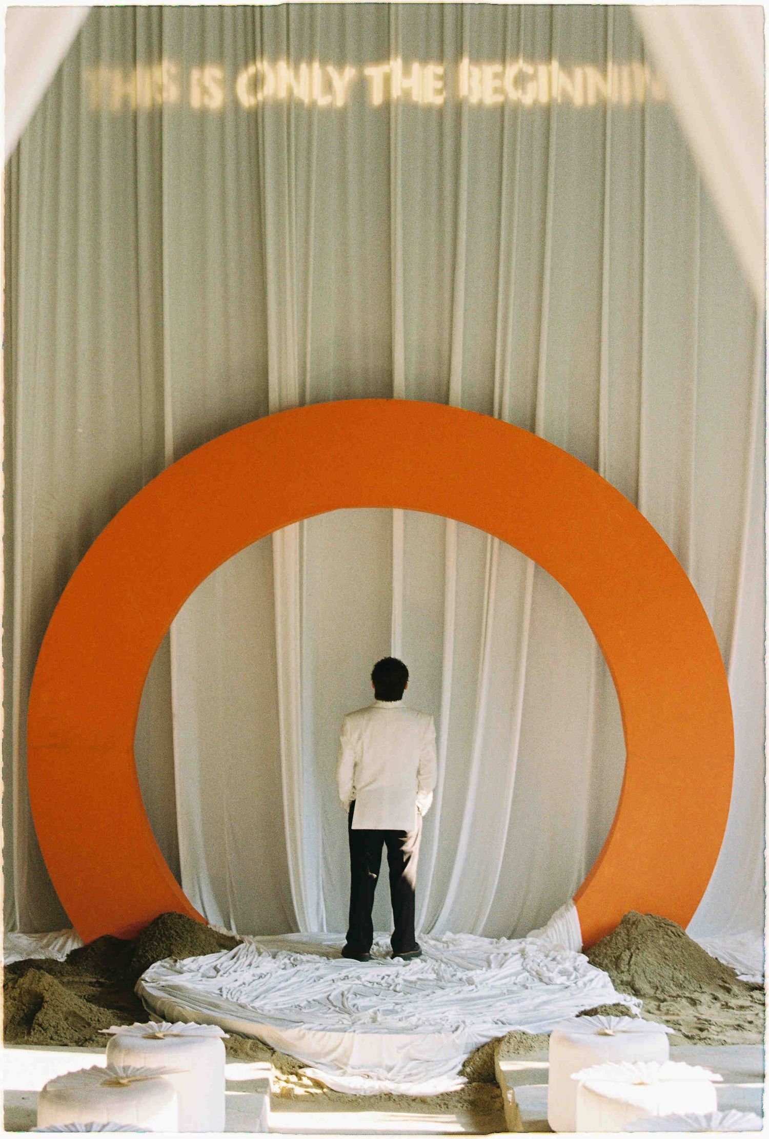Person standing before an orange circular arch installation with 'This Is Only The Beginning' text above.