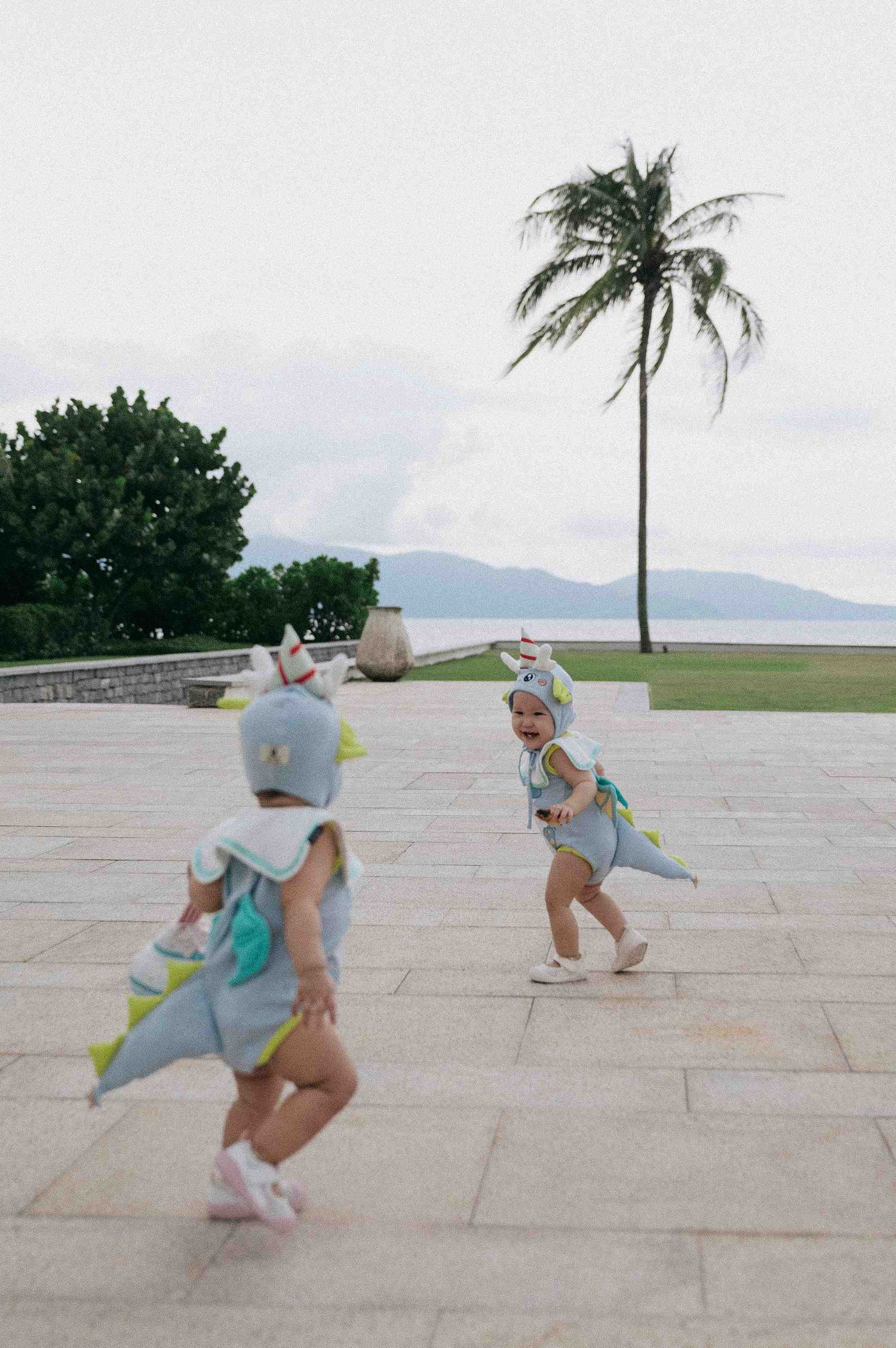 Da Nang family: small child in light blue outfit plays energetically on an outdoor patio, by AnhVuWedding.