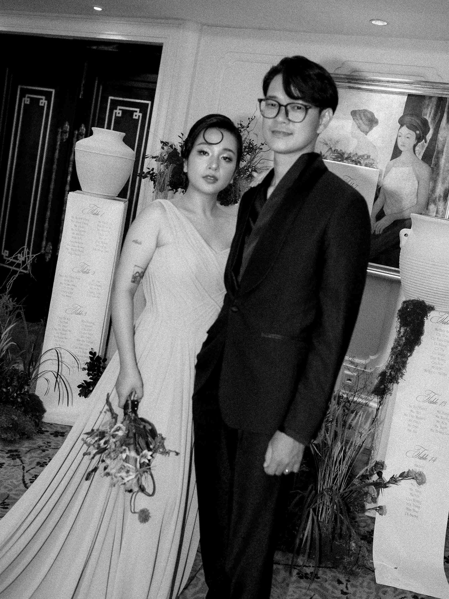 Black and white photo of wedding couple posing, woman in white gown, man in dark suit.