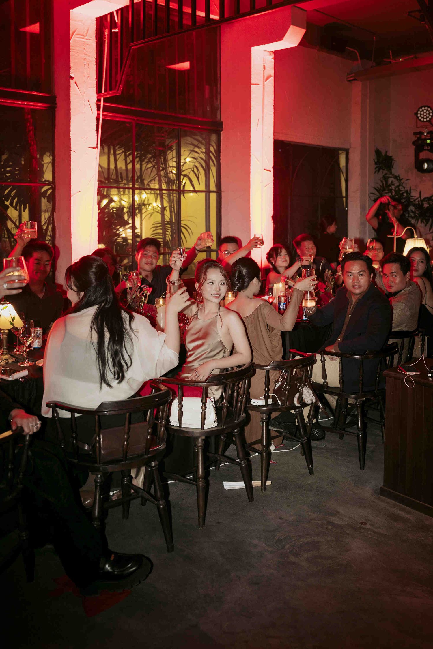 Guests raising glasses in a dimly lit bar with red lighting during a lively evening social gathering.