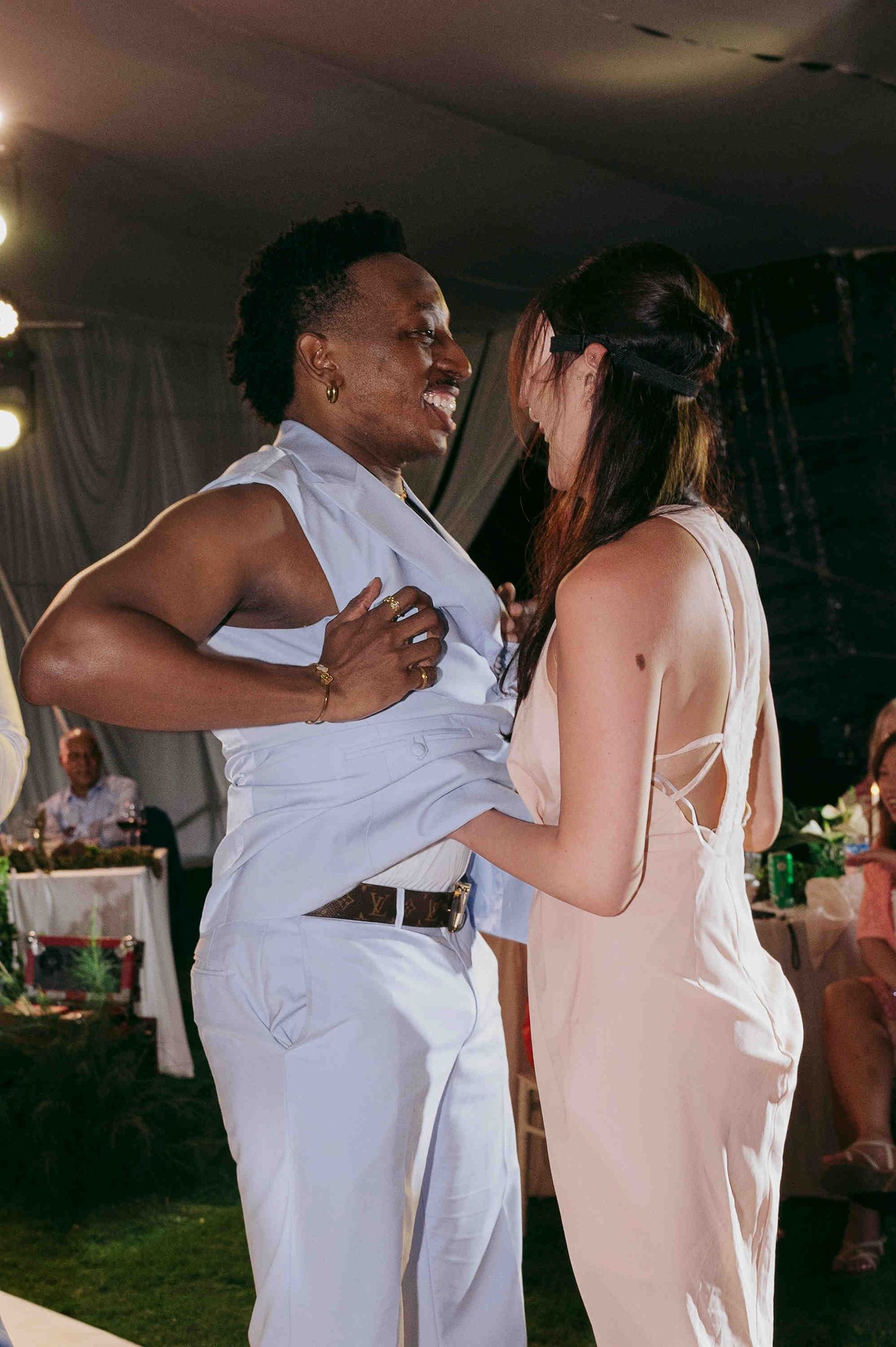 Couple dancing together at an outdoor evening wedding reception, wearing white and blush formal attire.