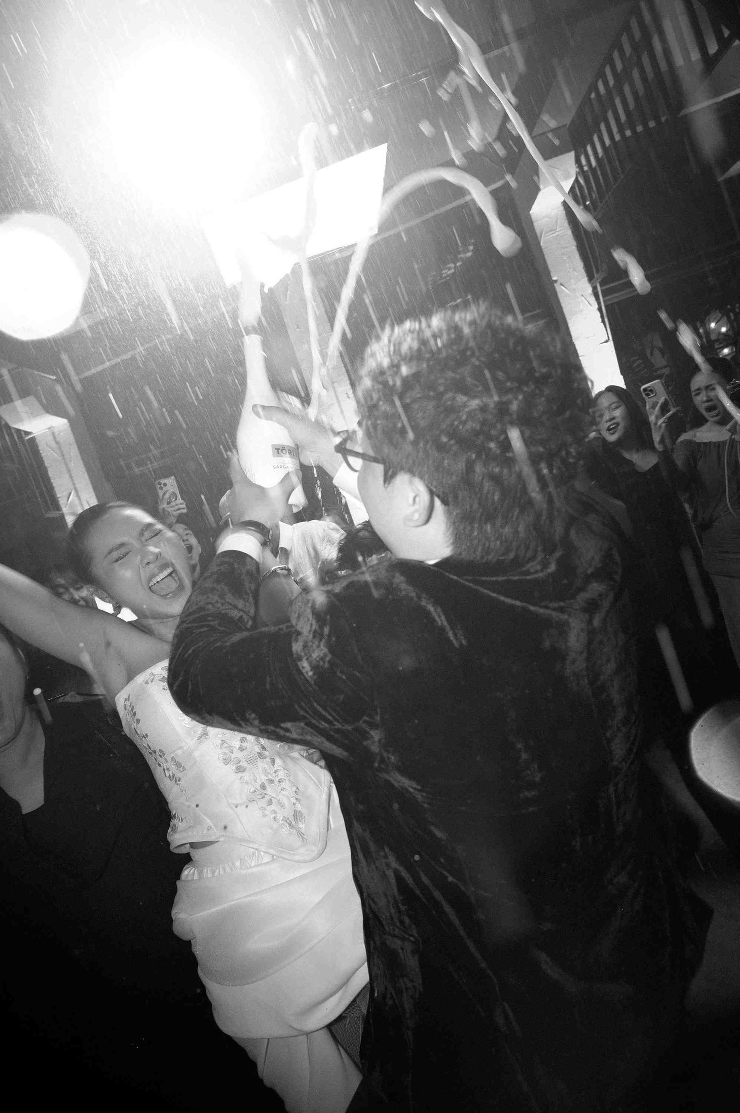 Black and white photo of a joyful couple dancing in the rain at a lively wedding reception celebration.