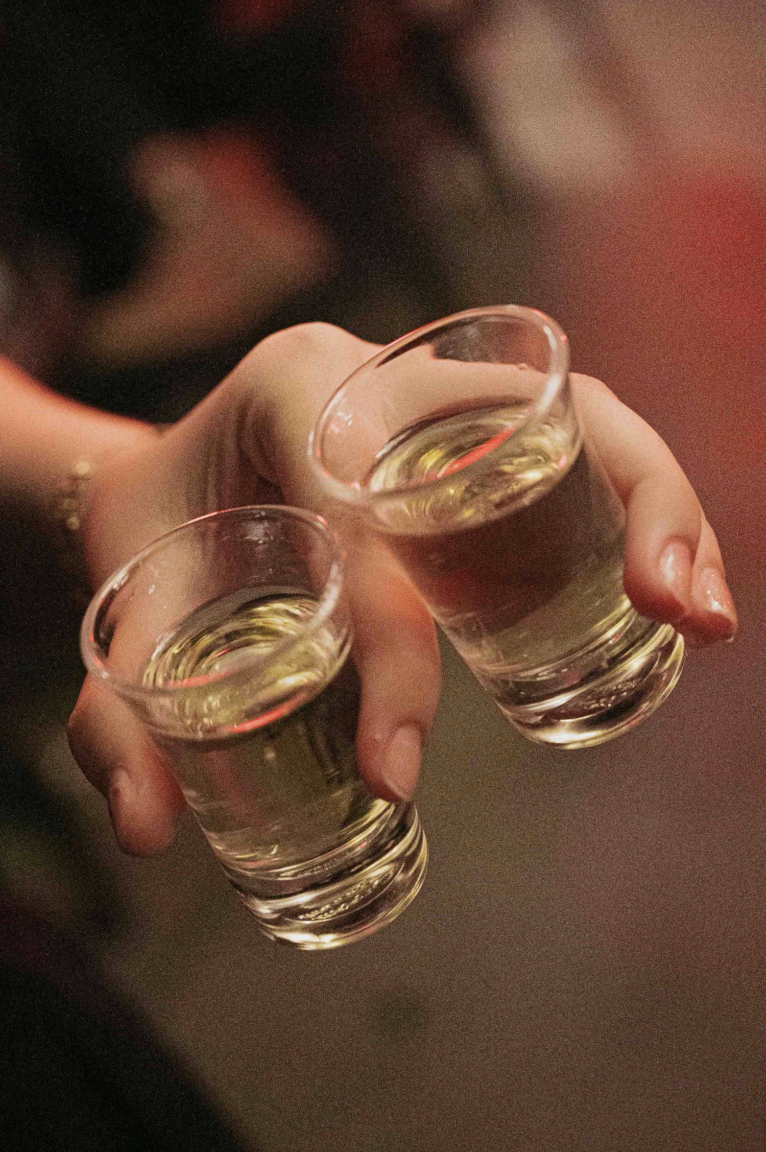 Hand holding three shot glasses filled with clear liquid at a party or bar celebration.