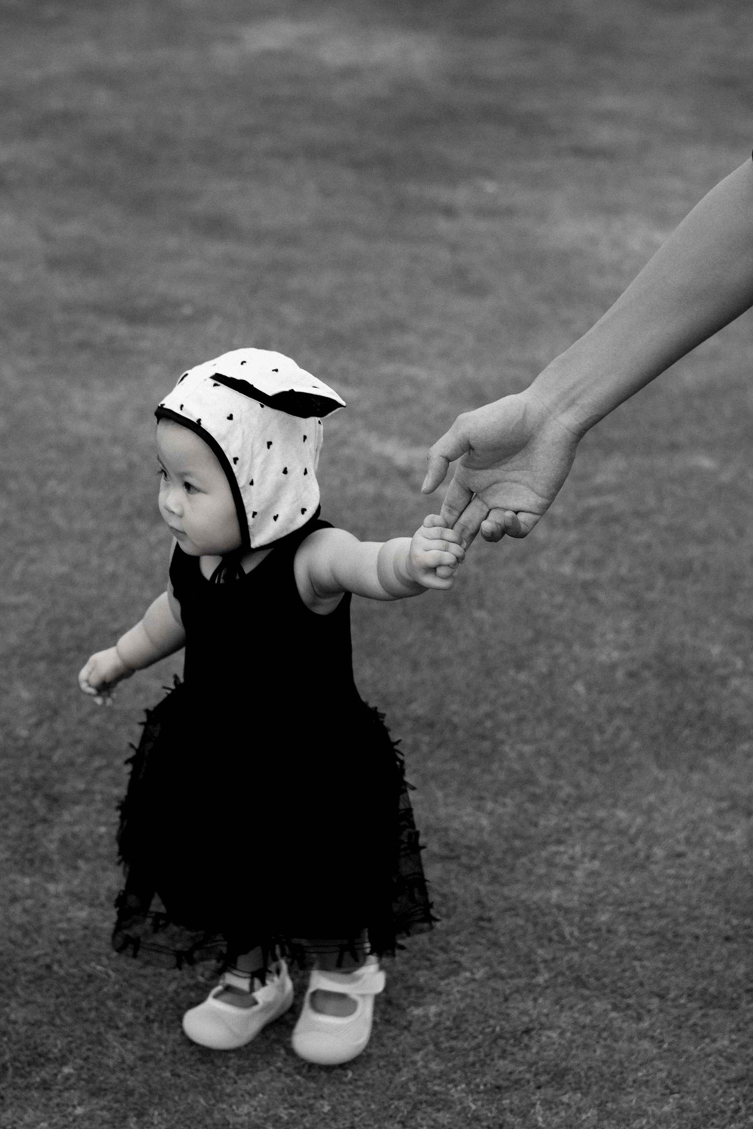 Da Nang family: black and white close-up of small shoes and hands on grass, by AnhVuWedding.
