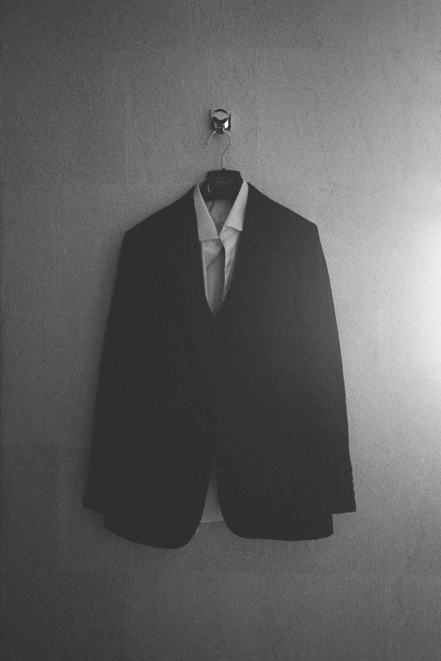 Lang Co wedding: black suit jacket and tie hanging against a plain gray background, by AnhVuWedding.