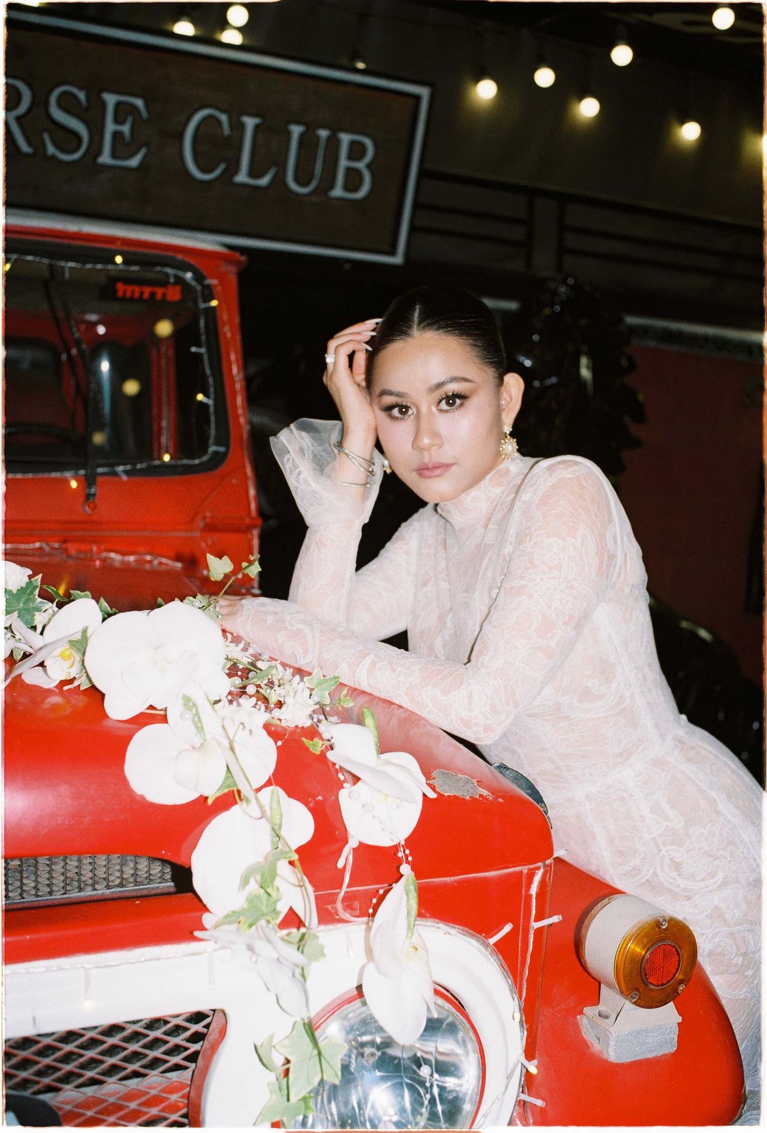 Saigon pre-wedding: artistic bridal poses with a vintage red vehicle and white flowers at a horse club, by AnhVuWedding.