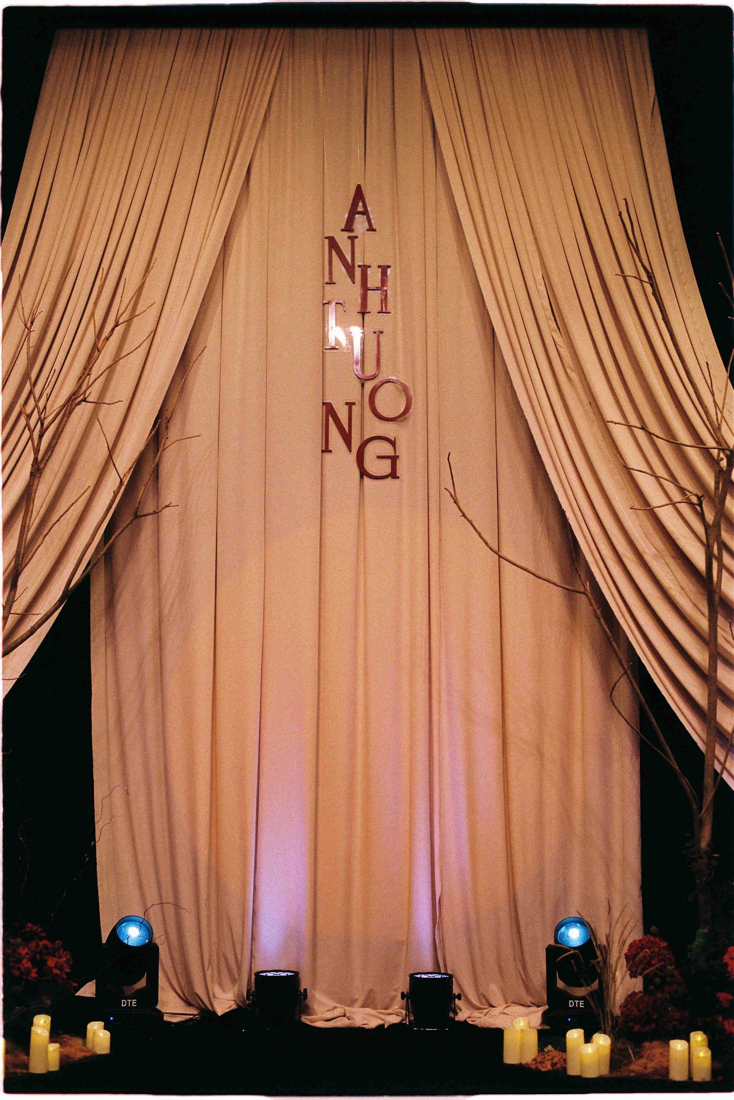 Elegant draped curtain backdrop with monogram letters and blue stage lights with candles at a wedding reception.