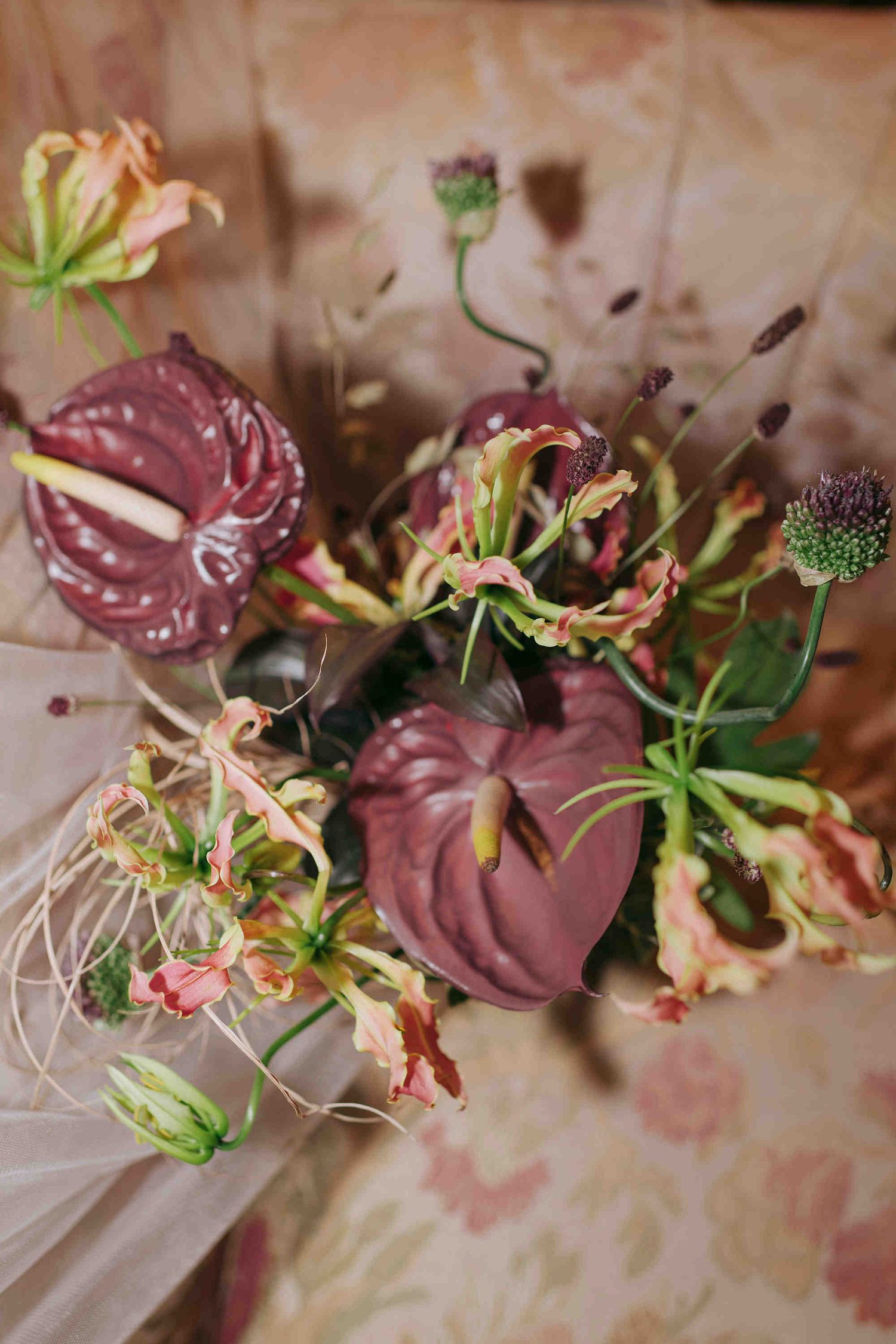 Elegant floral arrangement featuring deep burgundy anthuriums, gloriosa lilies, and scabiosa in rich autumn tones.
