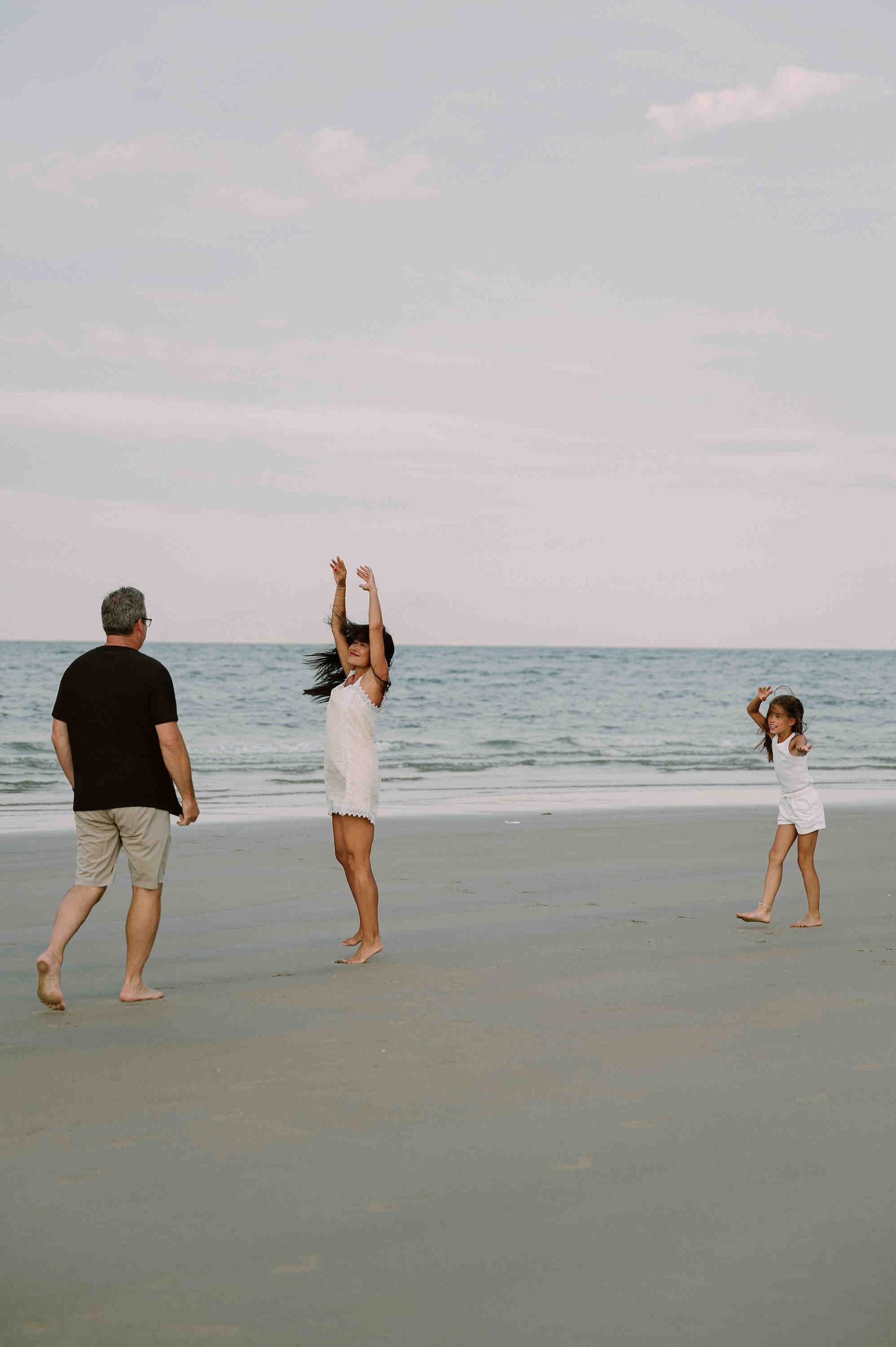 Da Nang family: a couple playfully running and dancing together on a cloudy beach by the ocean, by AnhVuWedding.