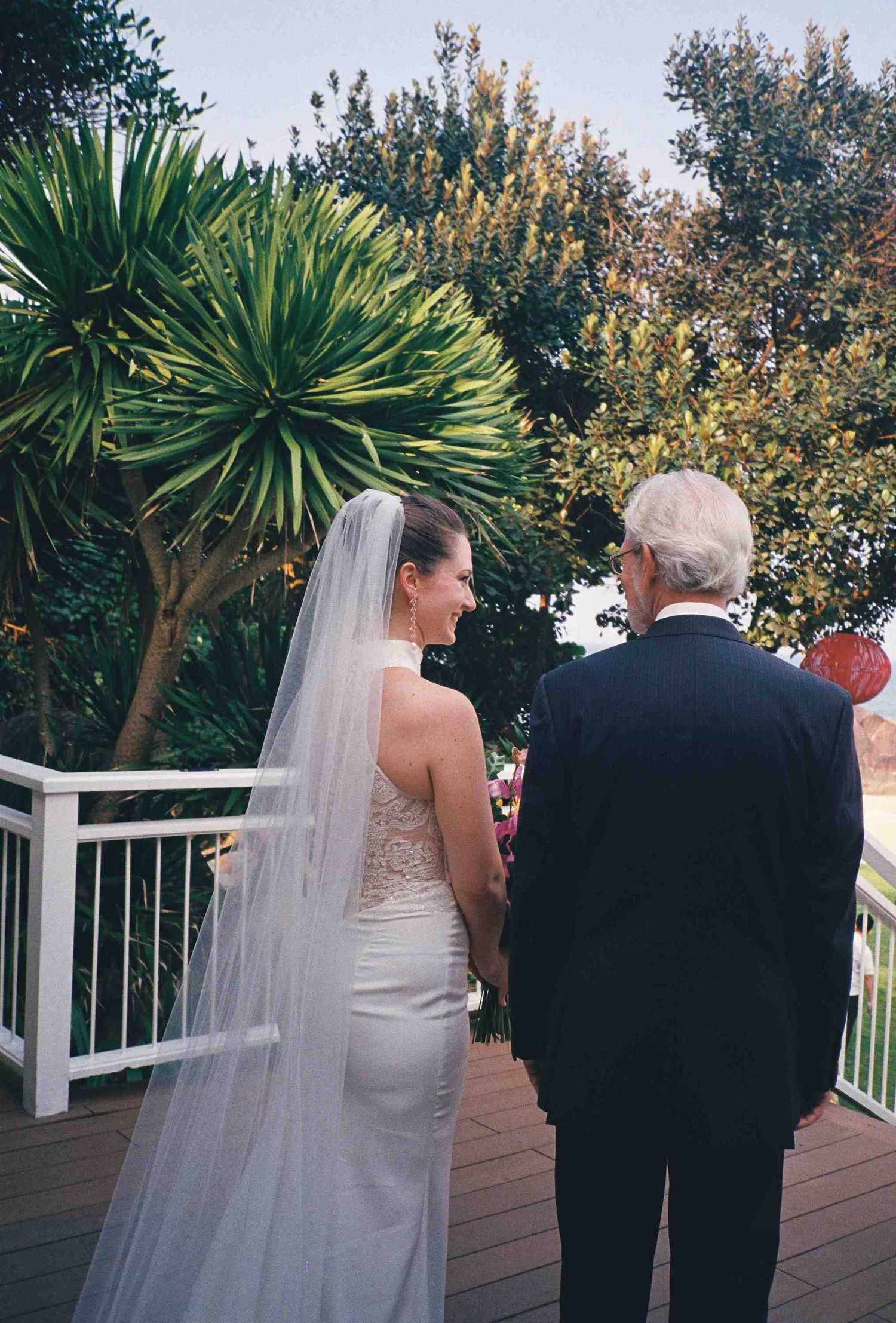 Lang Co wedding: wedding party walking along outdoor deck surrounded by tropical plants, by AnhVuWedding.