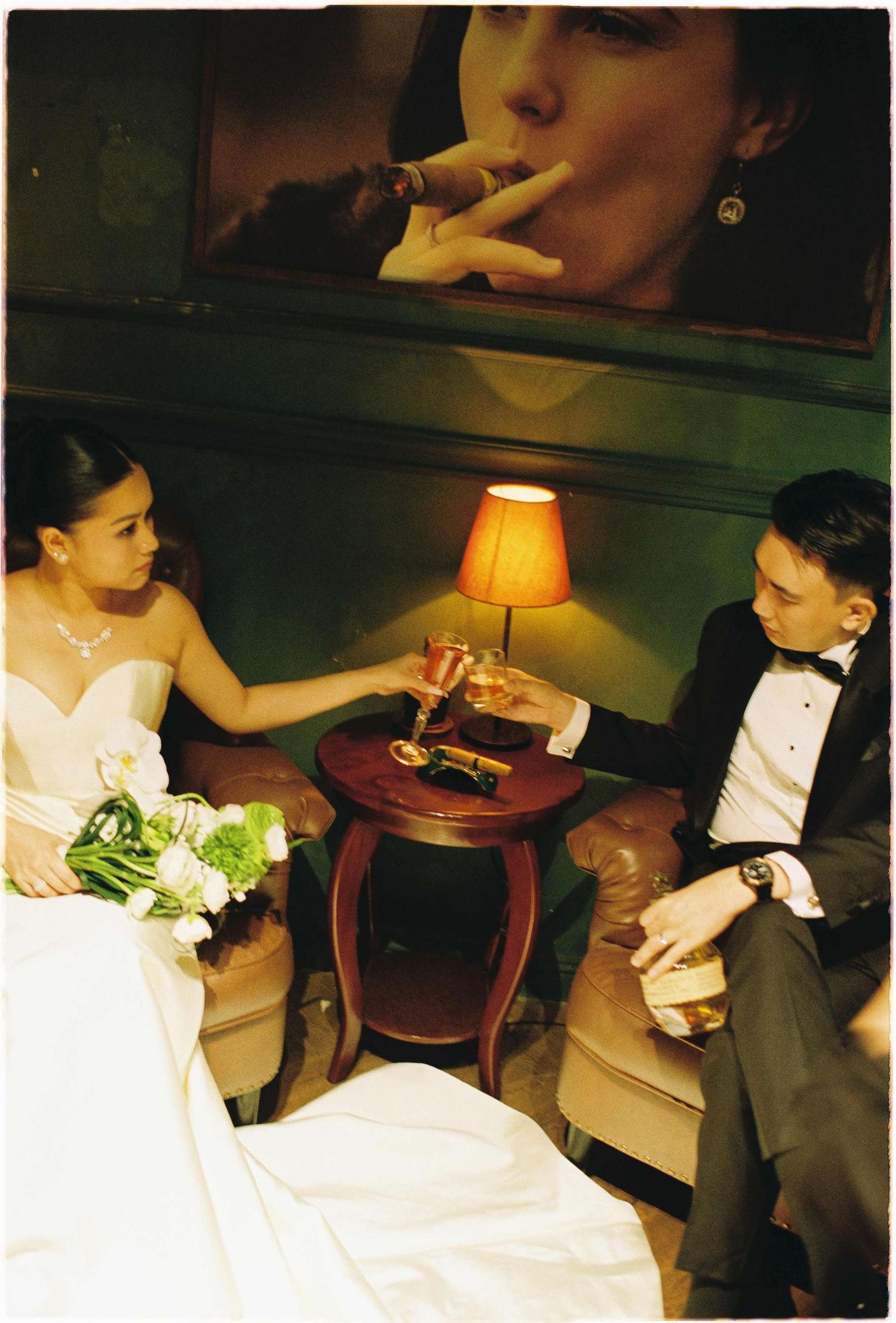Vietnam pre-wedding: elegant couple sharing drinks at small table with bouquet and mood lighting, by AnhVuWedding.