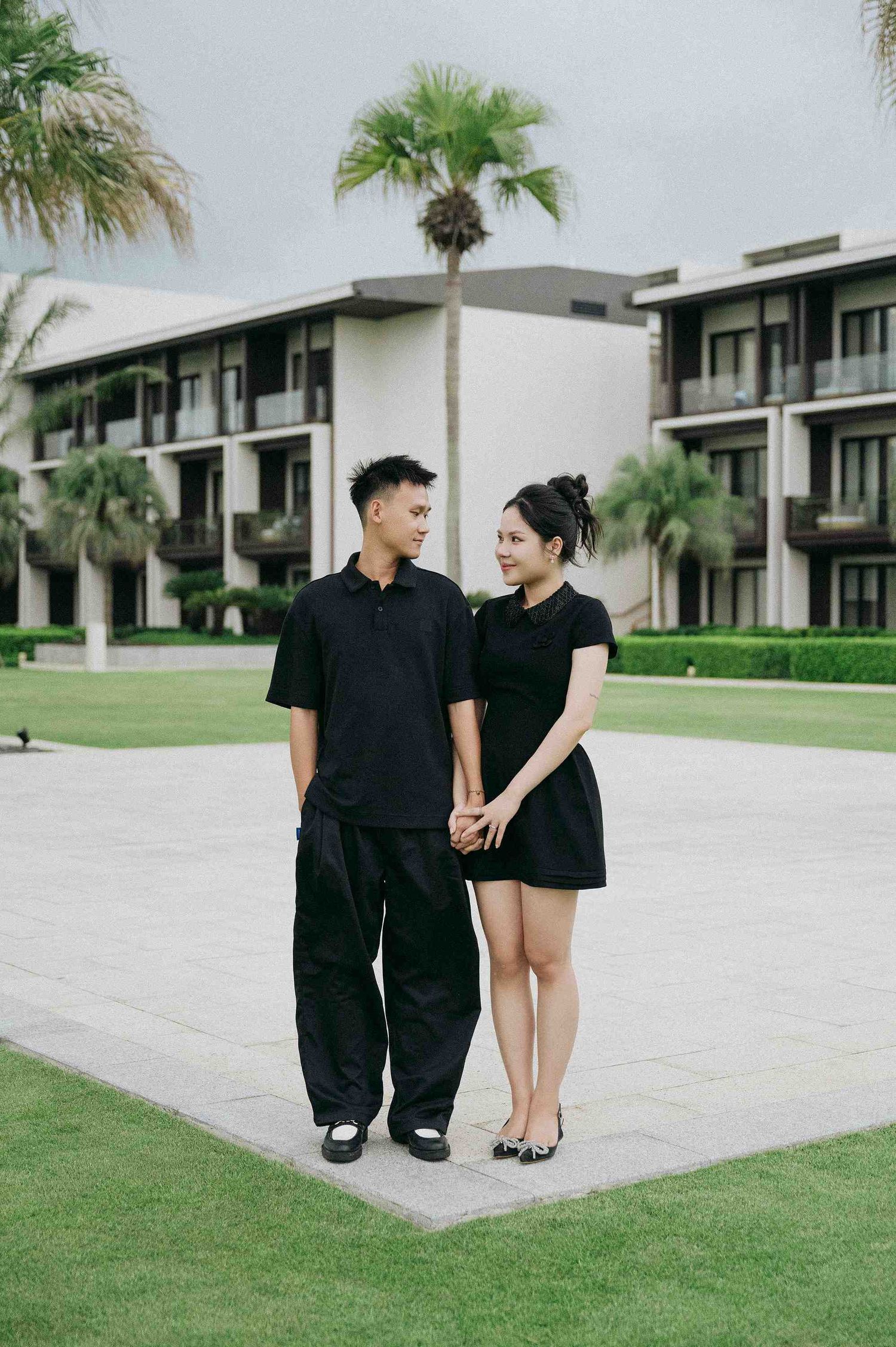 Da Nang family: people in black outfits walking and posing together on resort grounds with palm trees, by AnhVuWedding.