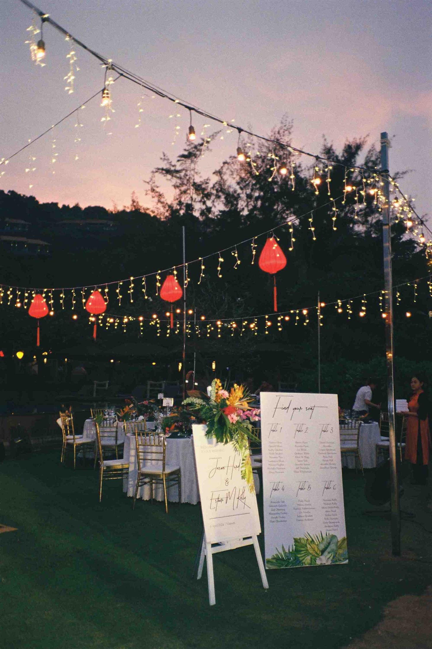 Lang Co wedding reception: reception setup with string lights and red lanterns at dusk under open sky, by AnhVuWedding.