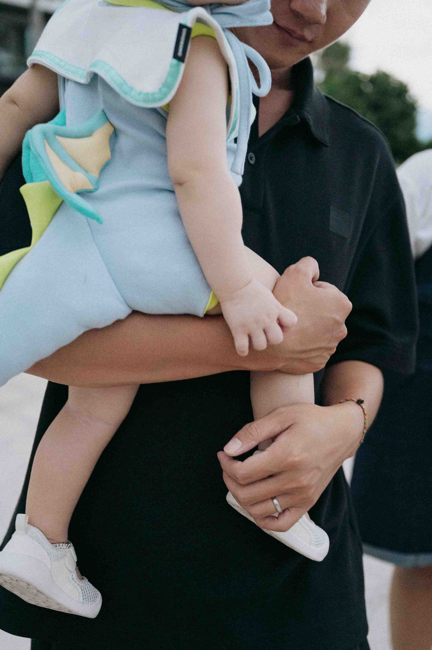 Da Nang family: close-up of a baby in light blue outfit being held by someone in black, by AnhVuWedding.
