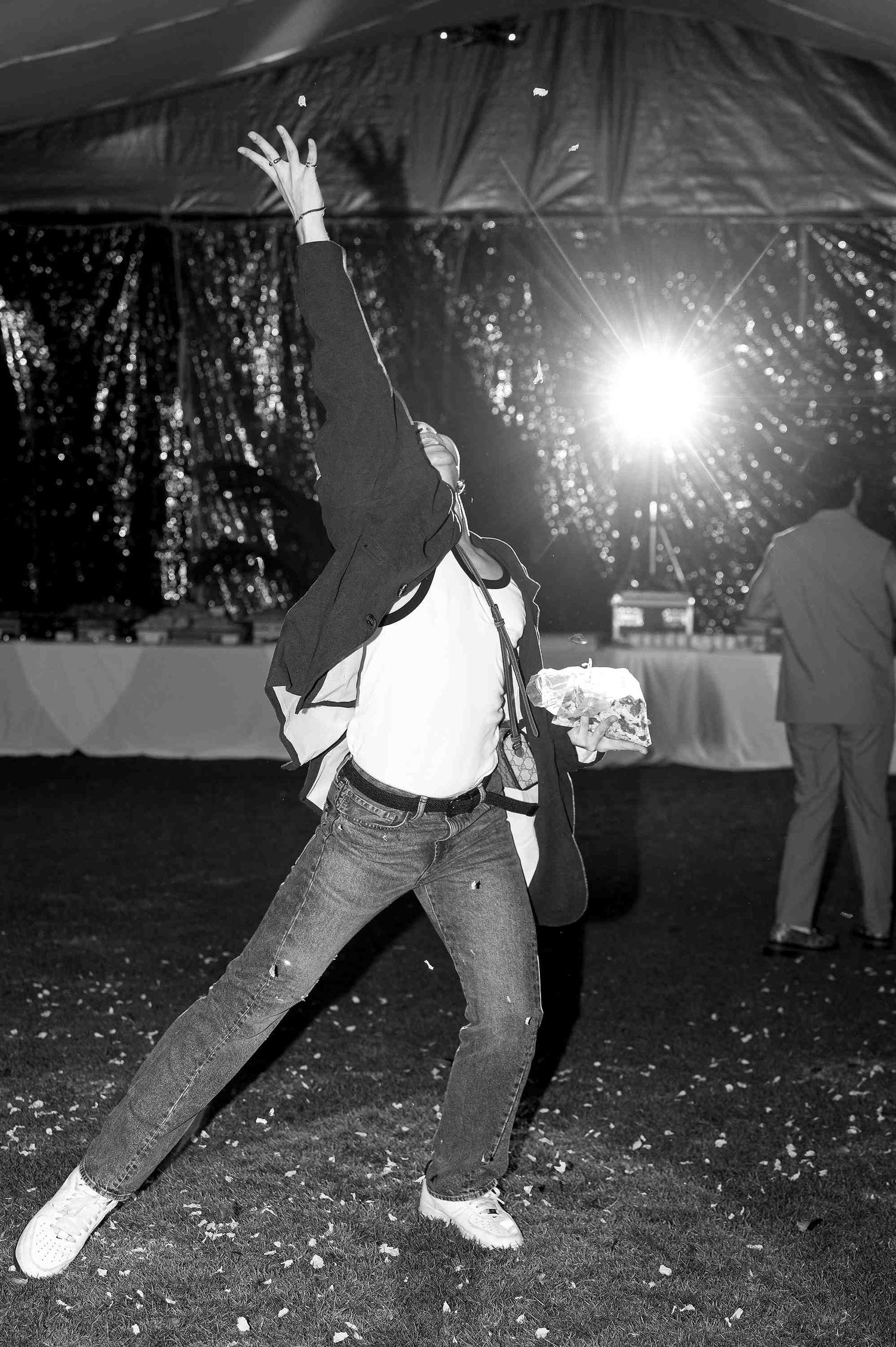 Person dancing energetically in black and white photo at a party under sparkly decorations with bright stage lighting.