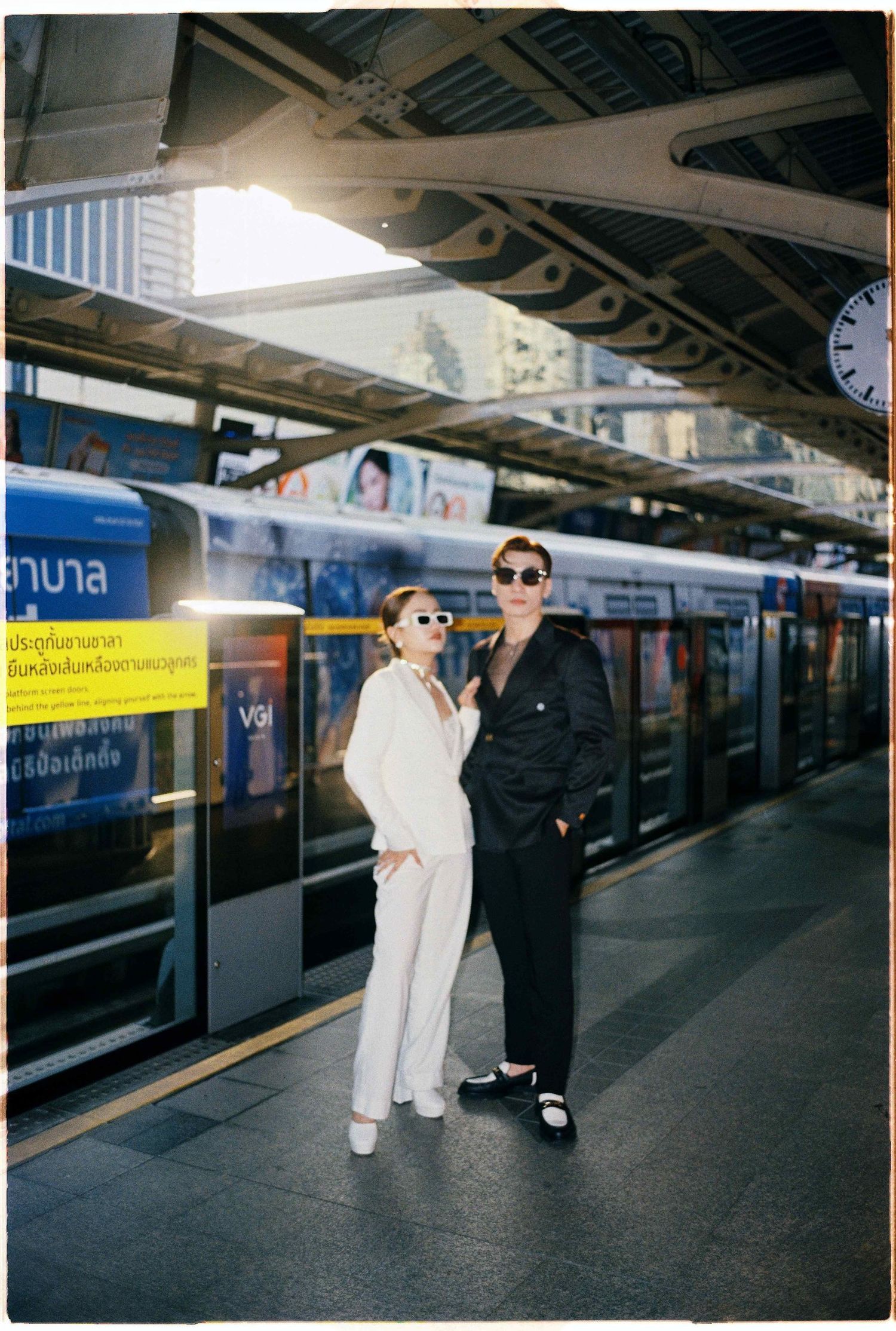 Saigon pre-wedding: couple in coordinated black and white outfits poses on a train platform, by AnhVuWedding.