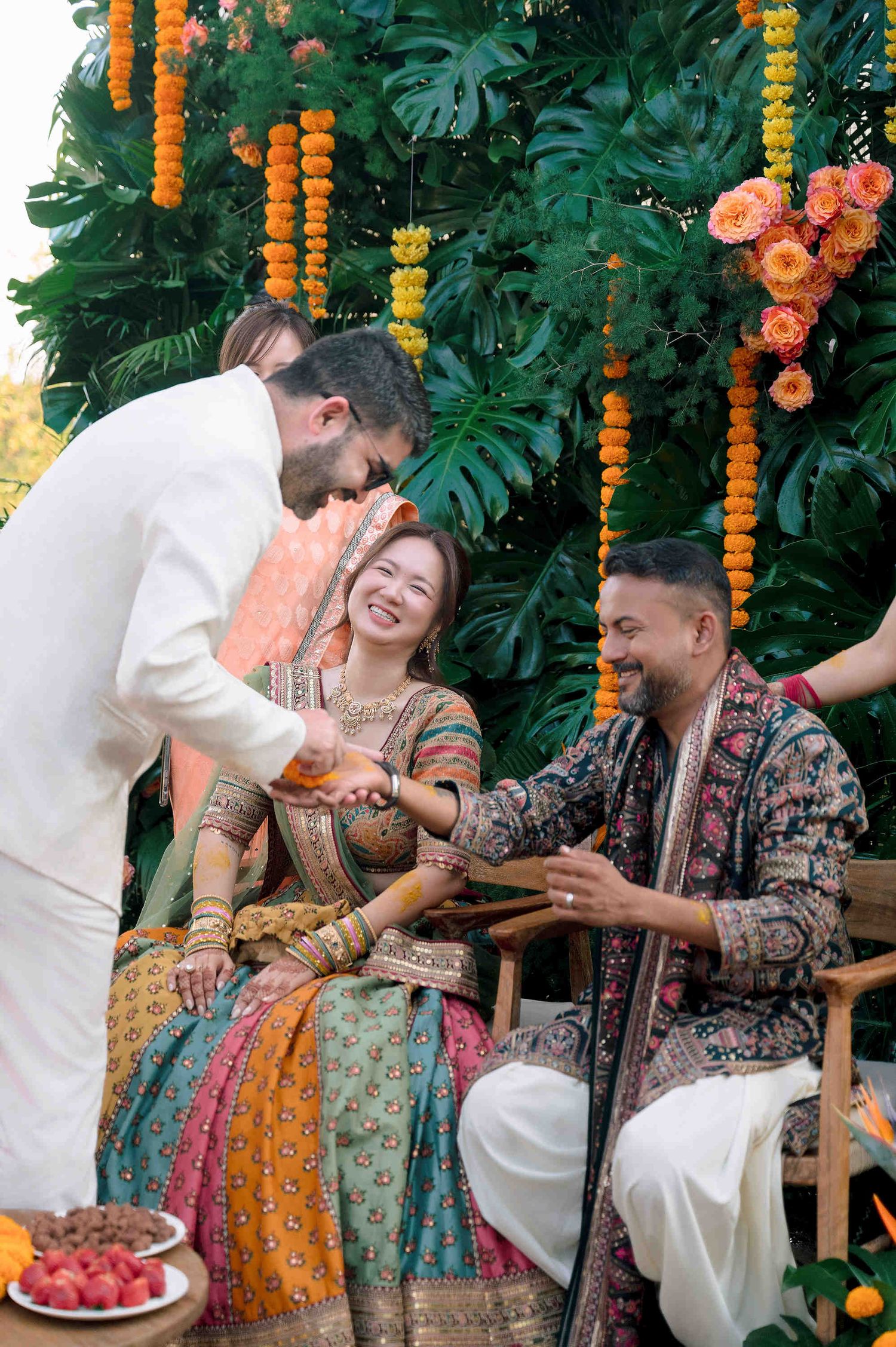 Bride in colorful lehenga smiles during Indian wedding ceremony with groom in traditional attire, marigold garlands backdrop.