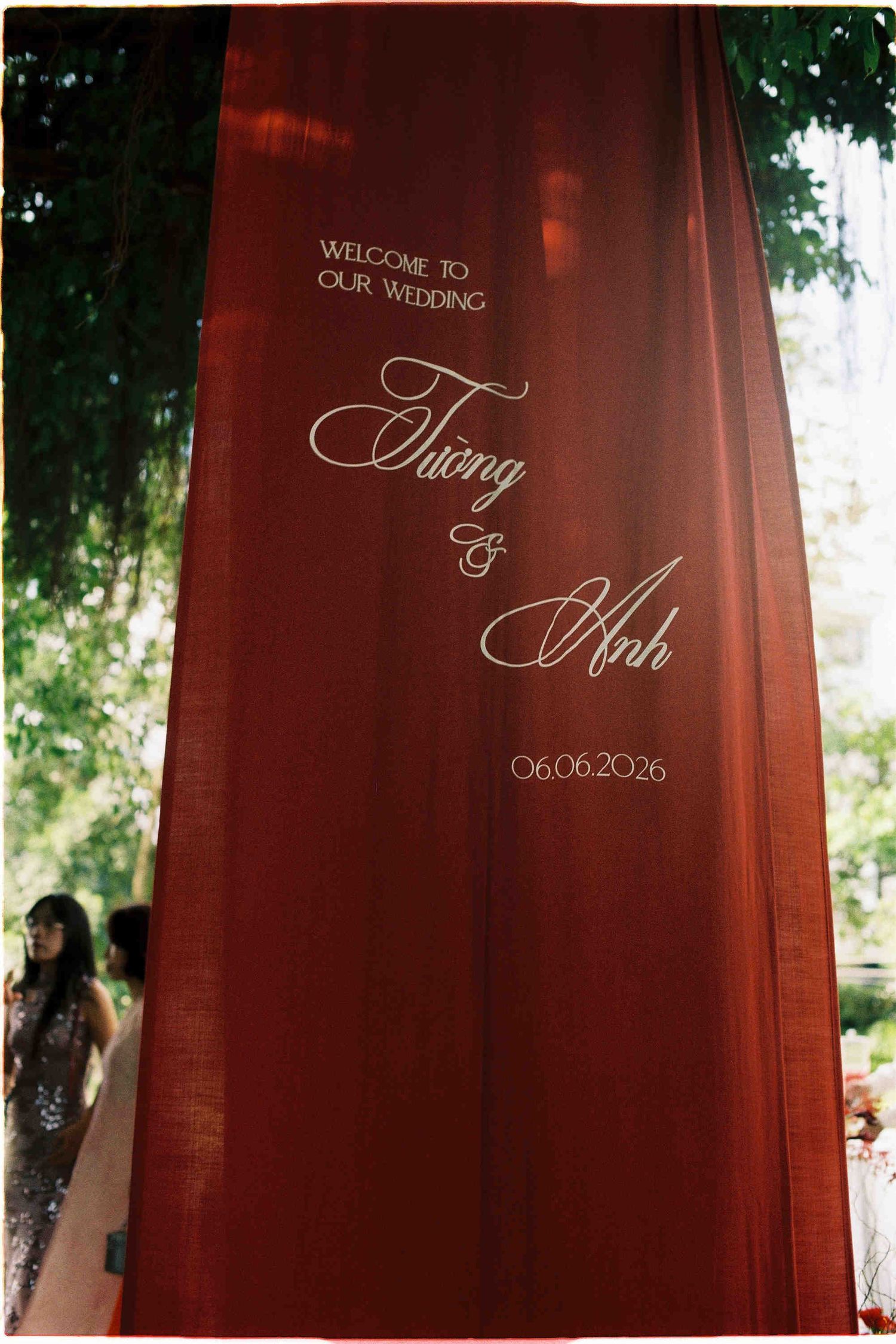 Elegant red draped wedding backdrop with white script reading Welcome to Our Wedding Tuong & Anh, dated 06.06.2026.