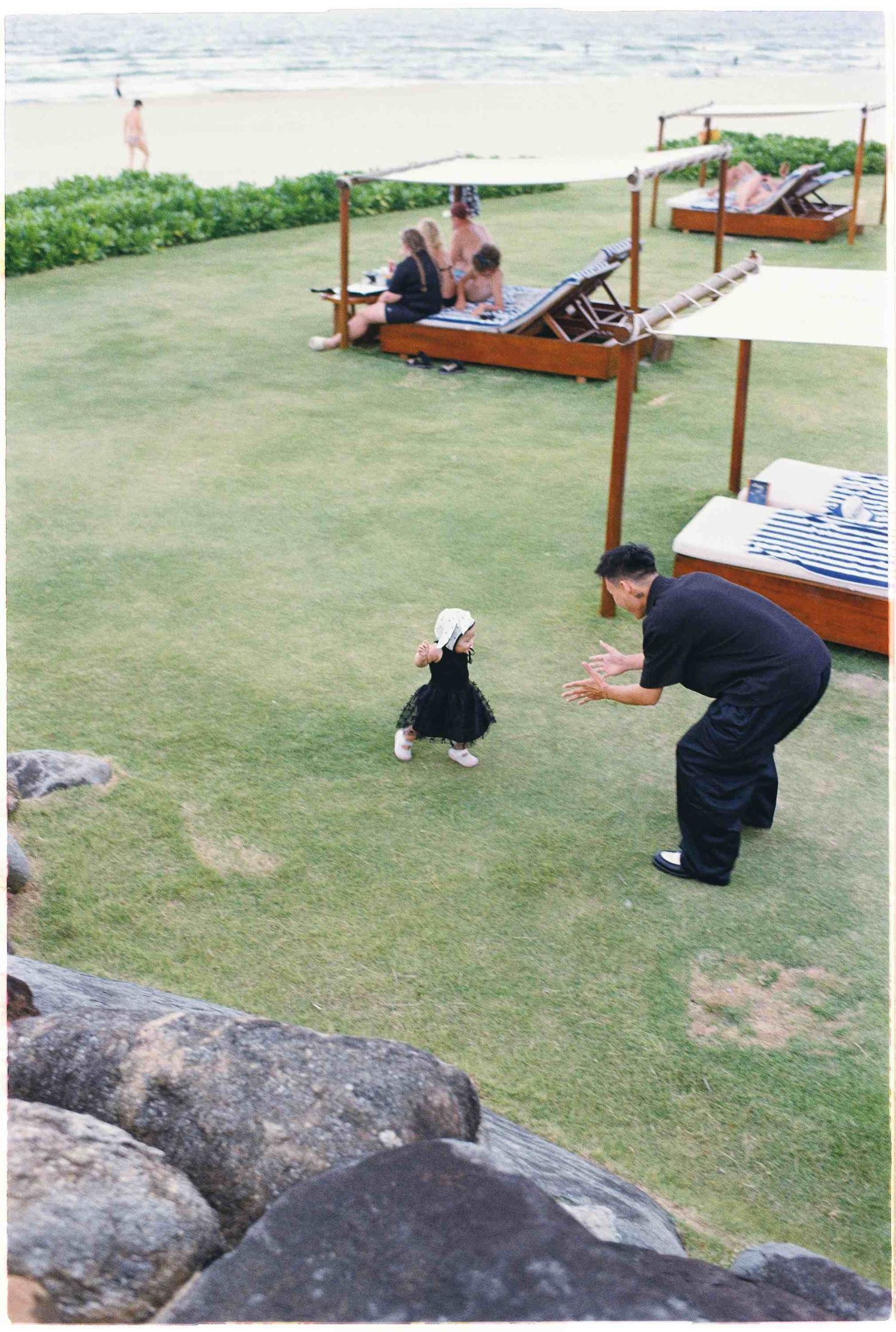 Da Nang family: people relax on outdoor lounge furniture near the ocean on a grassy lawn, by AnhVuWedding.