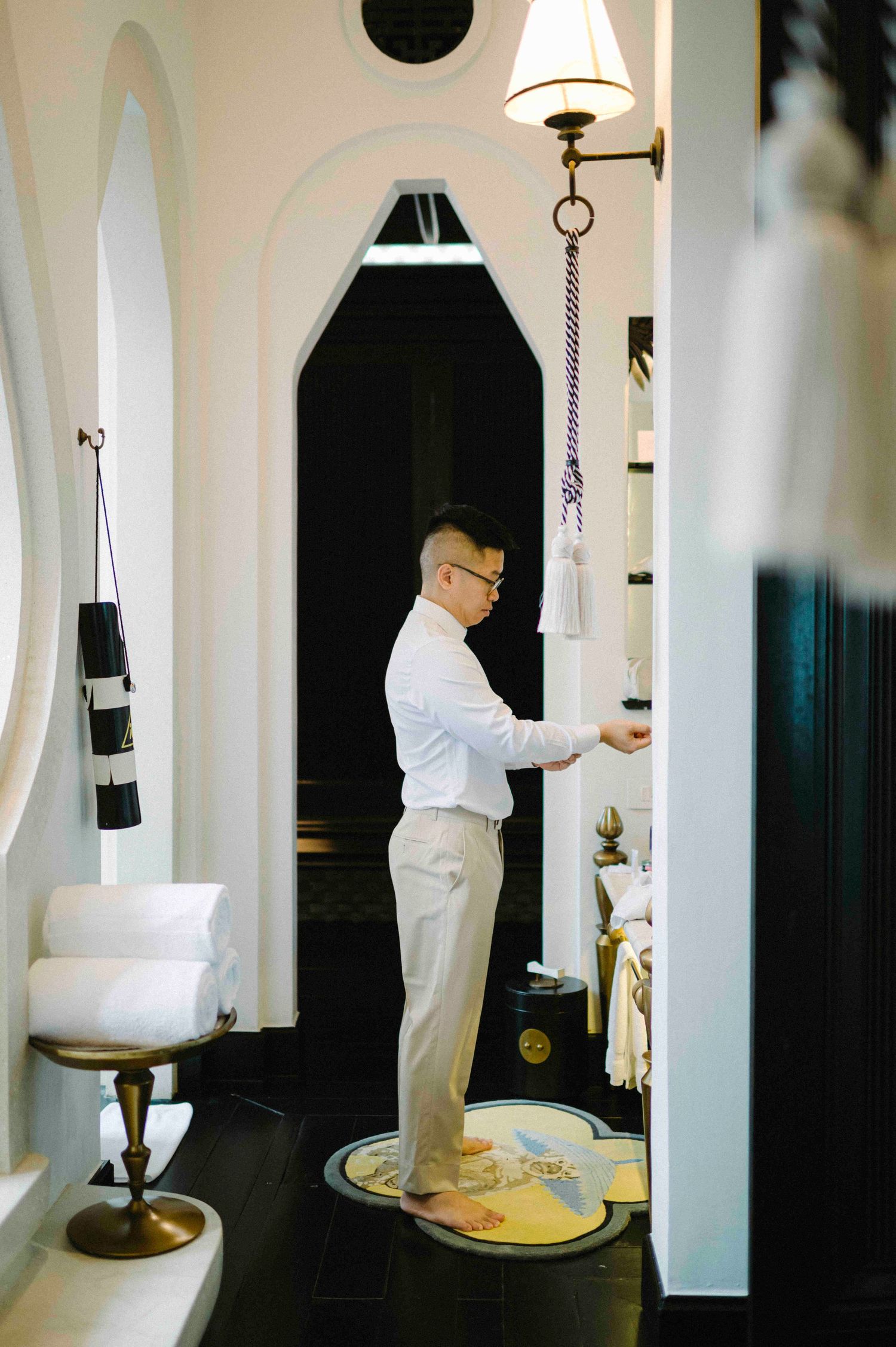 Da Nang photo: man in white shirt and trousers standing in elegant black and white interior hallway with arched doorways, by AnhVuWedding.