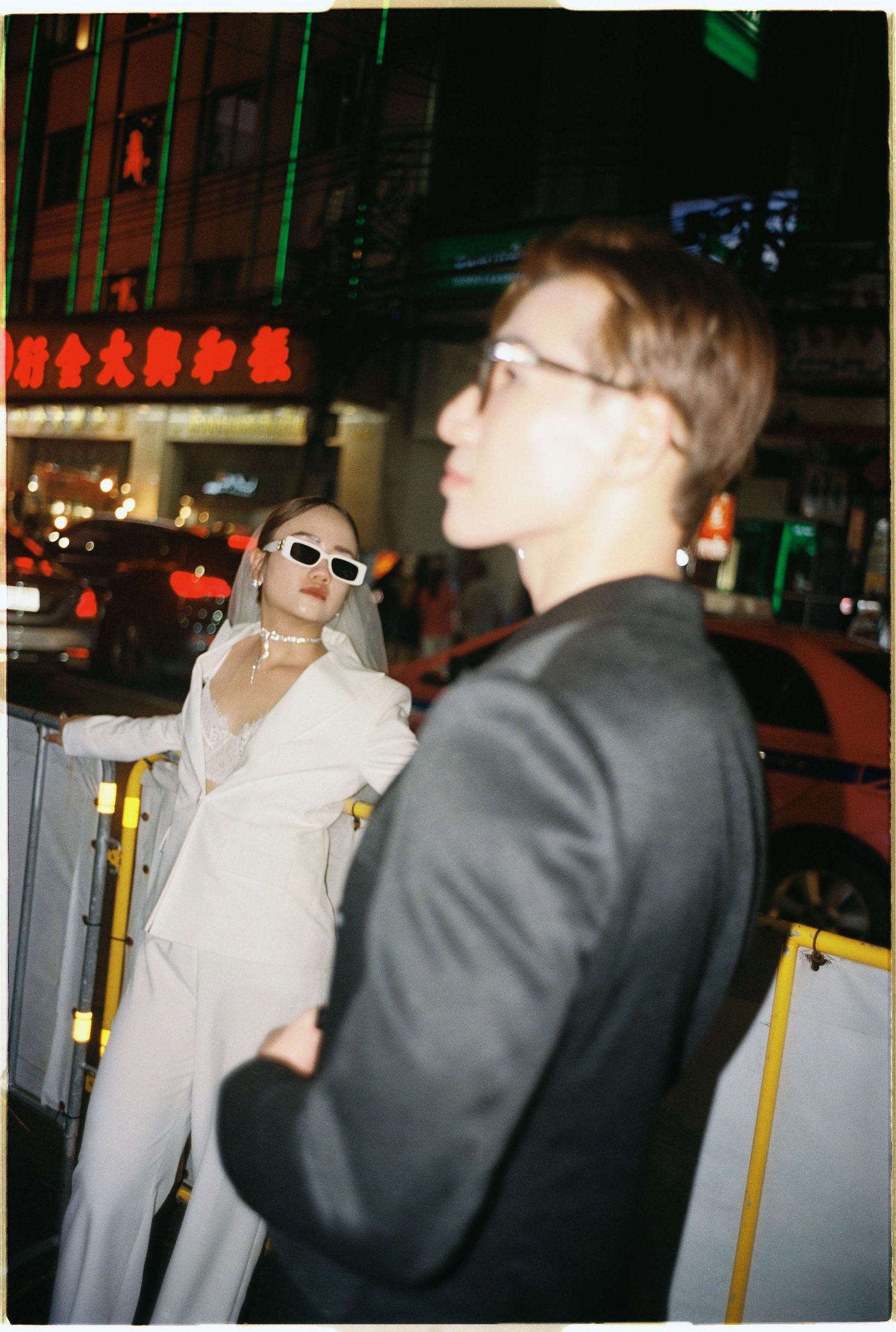 Saigon pre-wedding: people in black and white outfits pose together near metal barriers on an urban street at night, by AnhVuWedding.