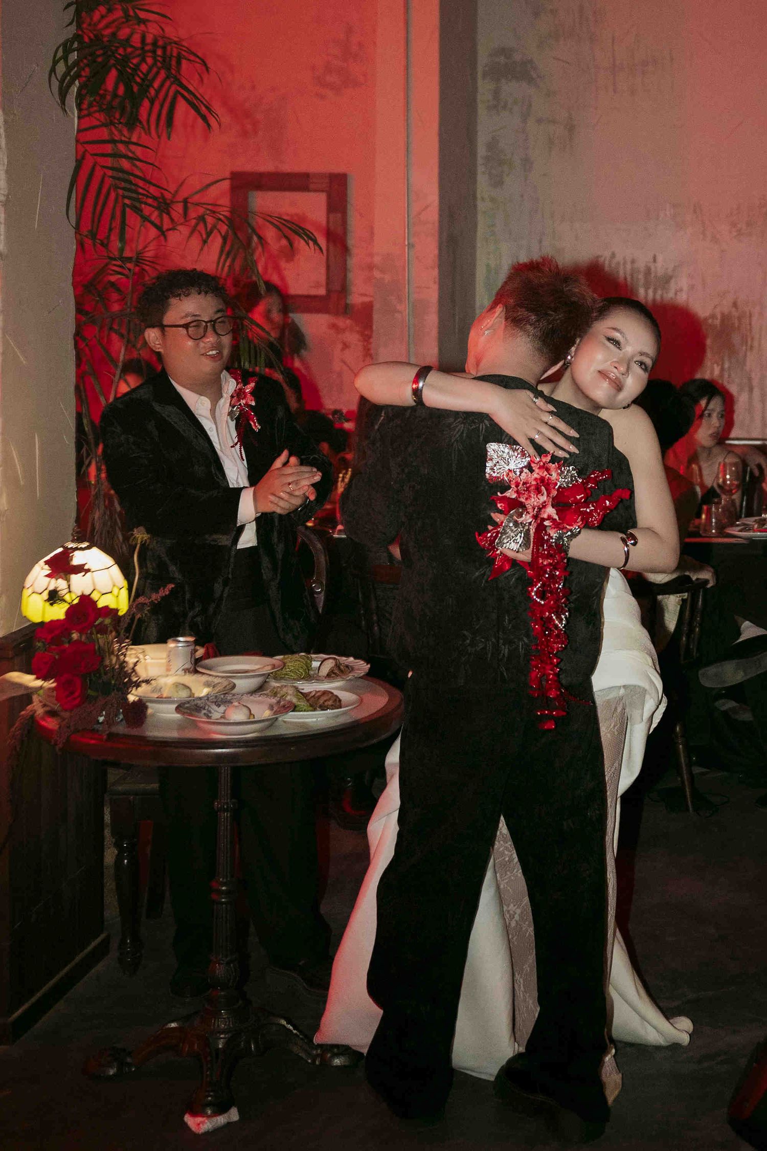 Couple shares an emotional hug on the dance floor at a wedding reception with red lighting.