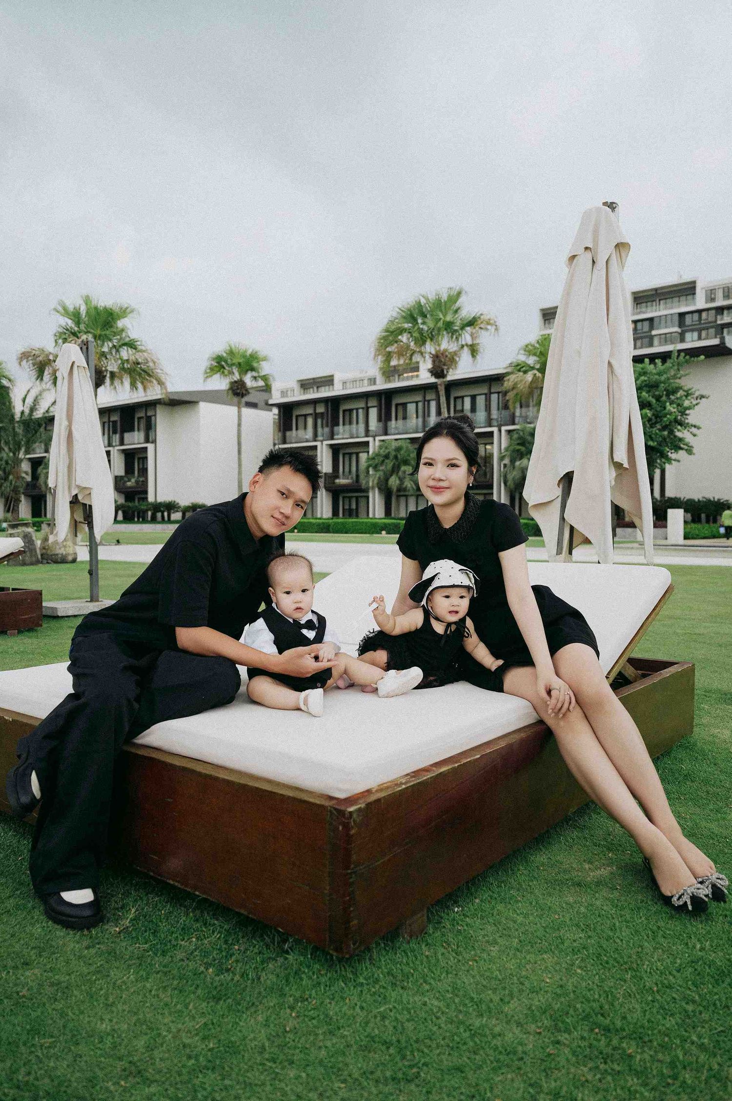 Da Nang family: family relaxing on an outdoor daybed with white cushions surrounded by palm trees, by AnhVuWedding.