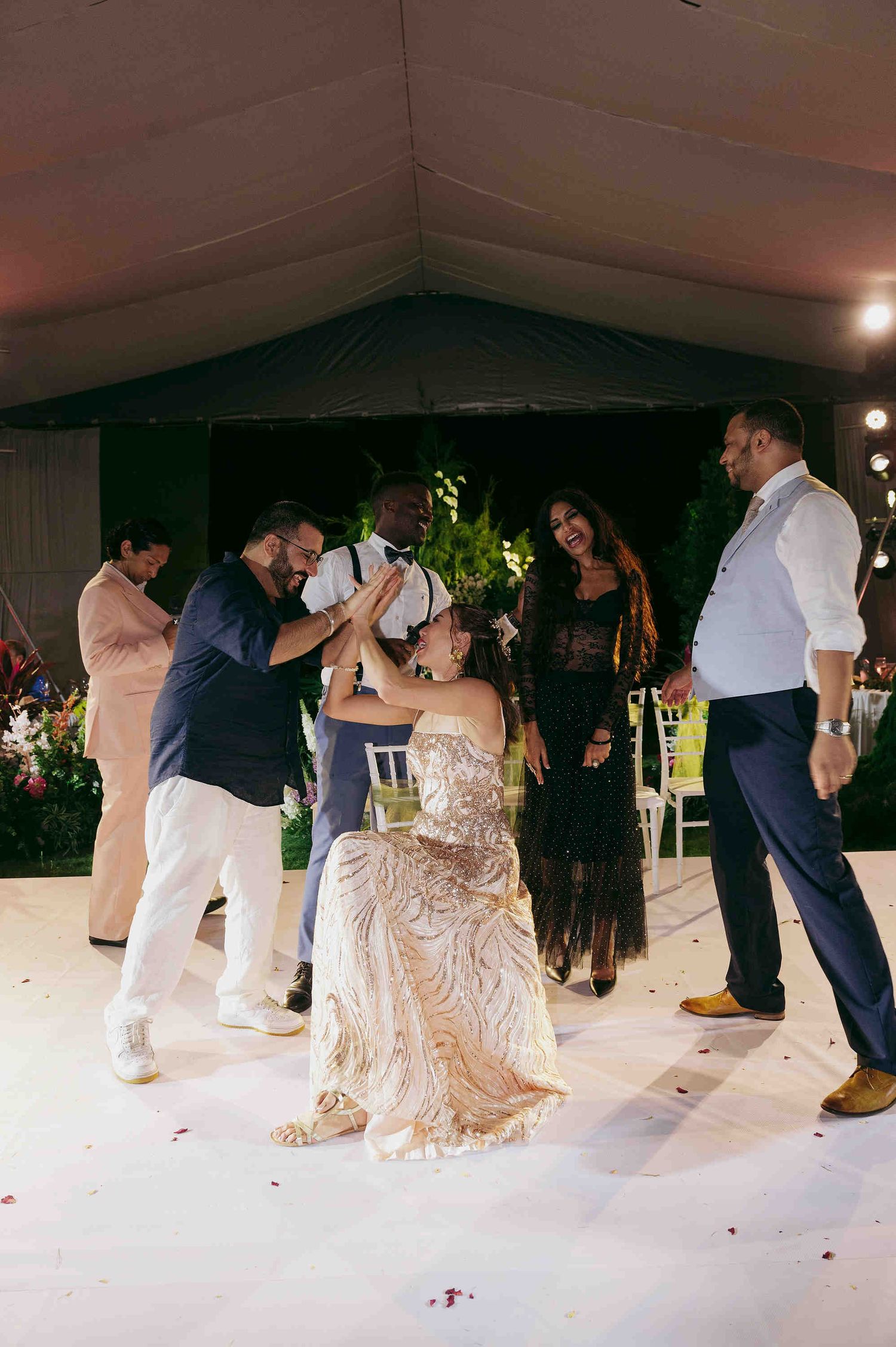 Wedding guests dance joyfully on a white dance floor under a tent at an elegant evening reception.
