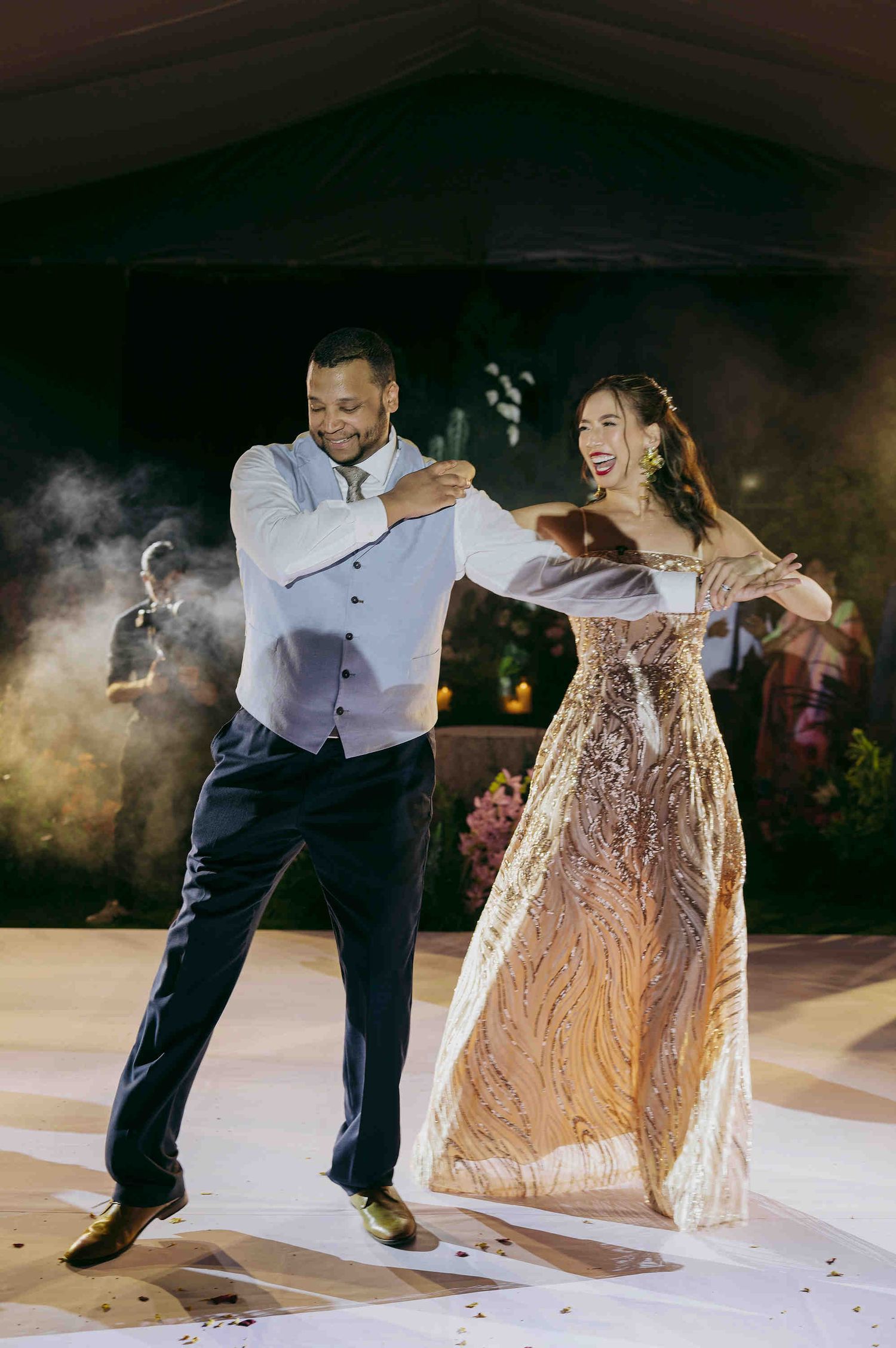 Bride and groom share a joyful first dance at their wedding reception, with the bride wearing a stunning gold gown.
