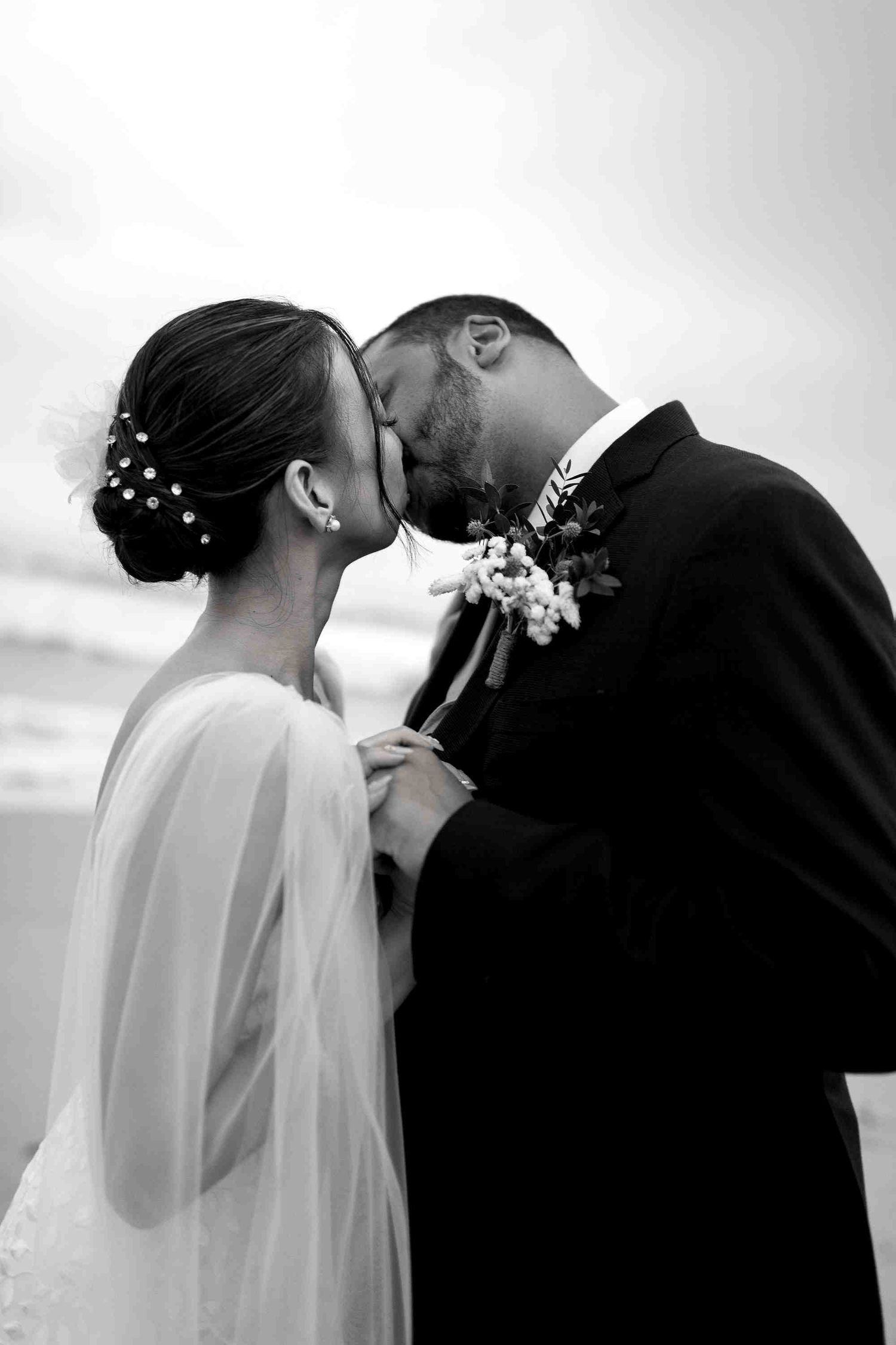Black and white photo of bride and groom sharing an intimate moment on a beach, touching foreheads.