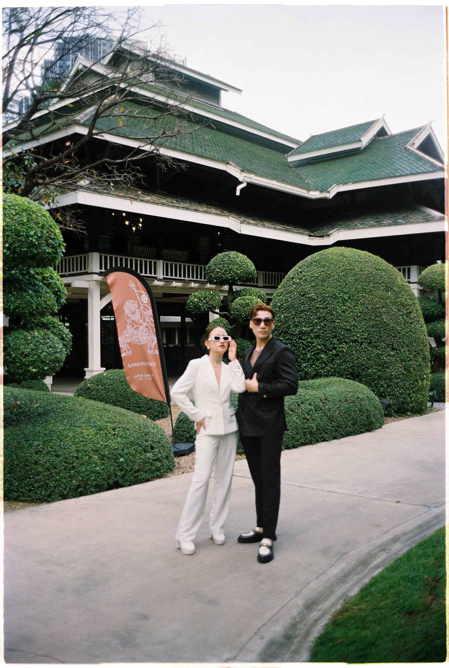 Saigon pre-wedding: two people in contrasting outfits dancing outside a traditional building with green roof, by AnhVuWedding.