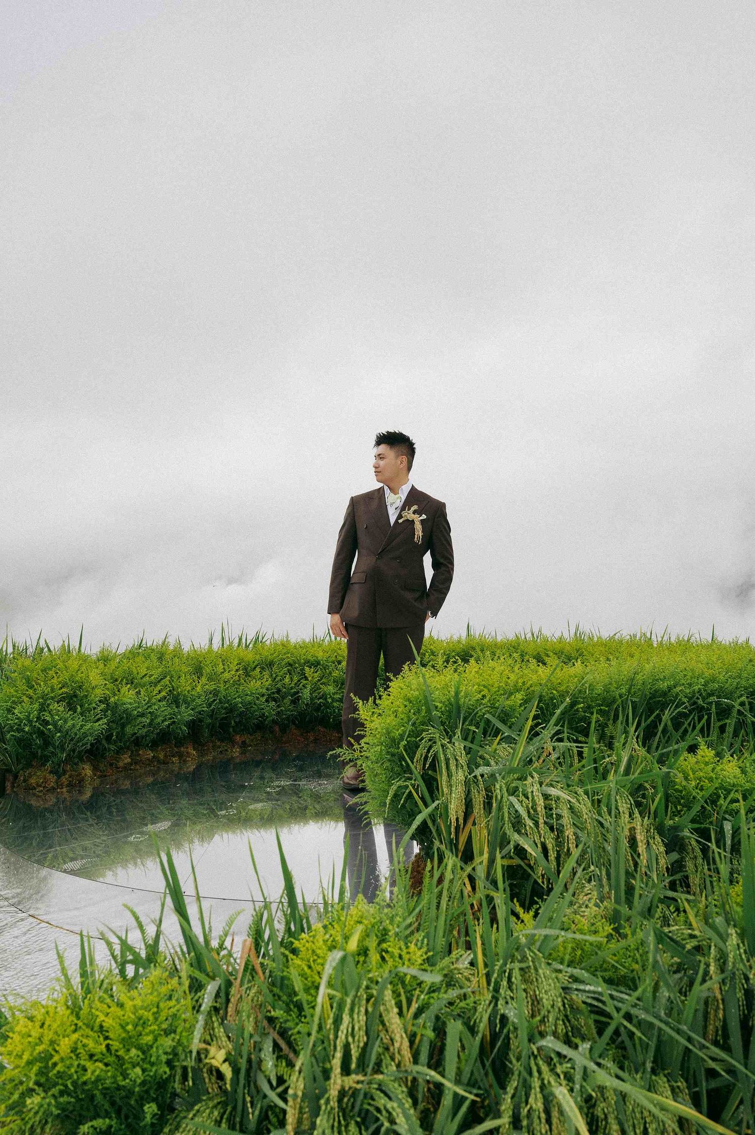 wedding: couple in wedding attire explores a scenic natural area with tall grasses and water, by AnhVuWedding.