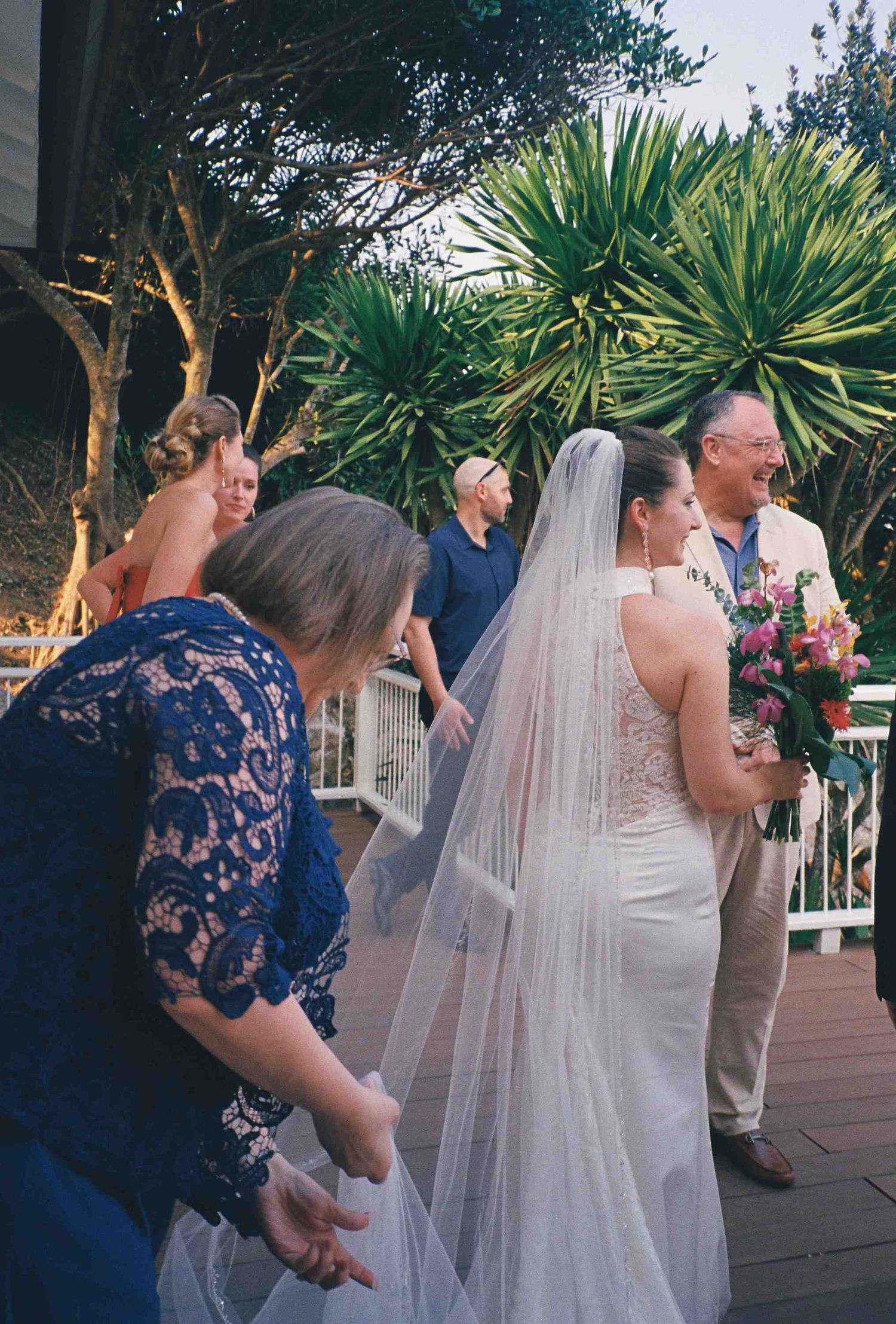 Lang Co wedding ceremony: wedding ceremony guests mingling on outdoor deck with tropical landscaping, by AnhVuWedding.