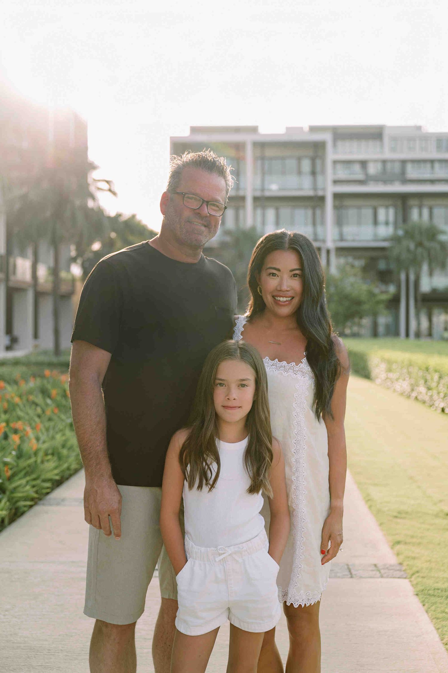 Da Nang family: family wearing black and white outfits walks together on a paved path near a beach during golden hour, by AnhVuWedding.