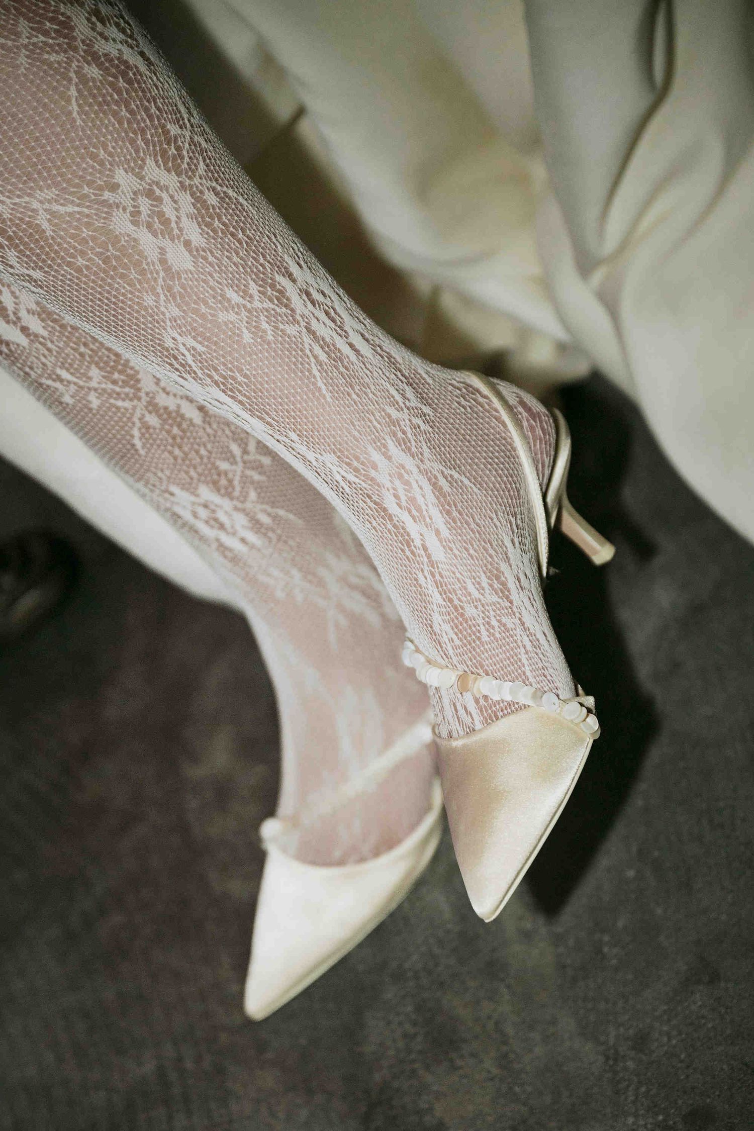 Elegant bridal look featuring white lace tights and pointed-toe satin kitten heels on a bride.