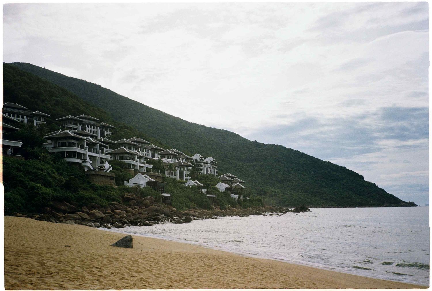 photo: beachfront buildings nestled on hillside overlooking sandy shore and ocean, by AnhVuWedding.