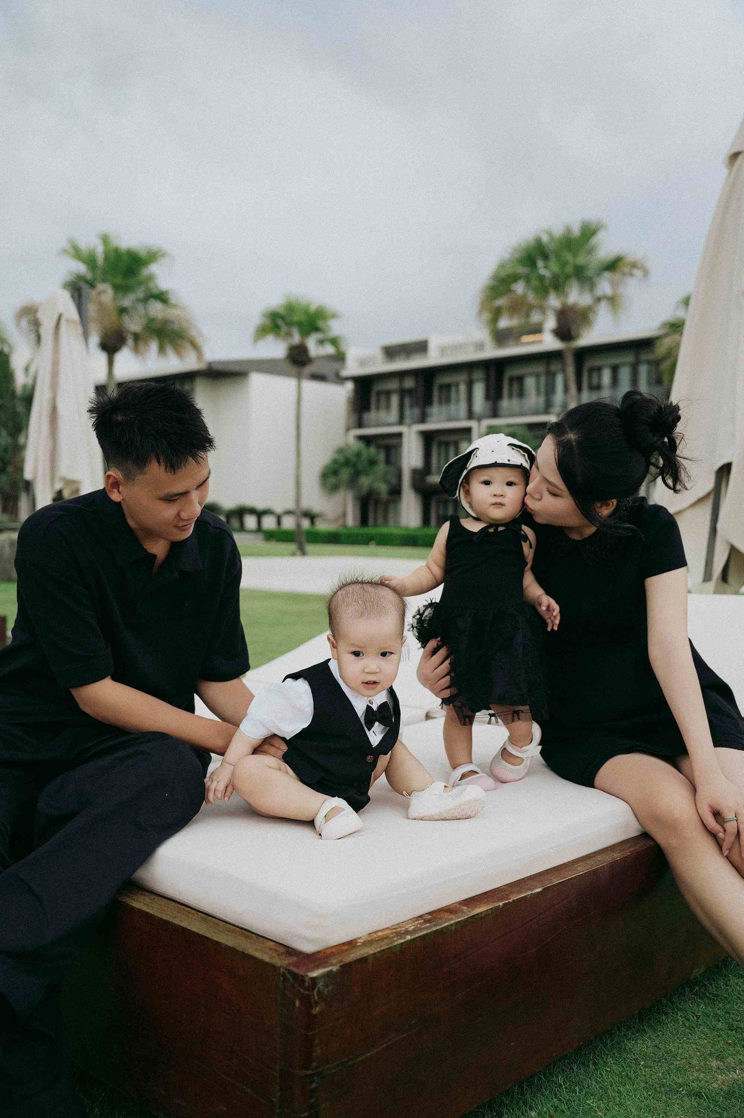 Da Nang family: family spending time together on a white outdoor lounger in a tropical setting, by AnhVuWedding.